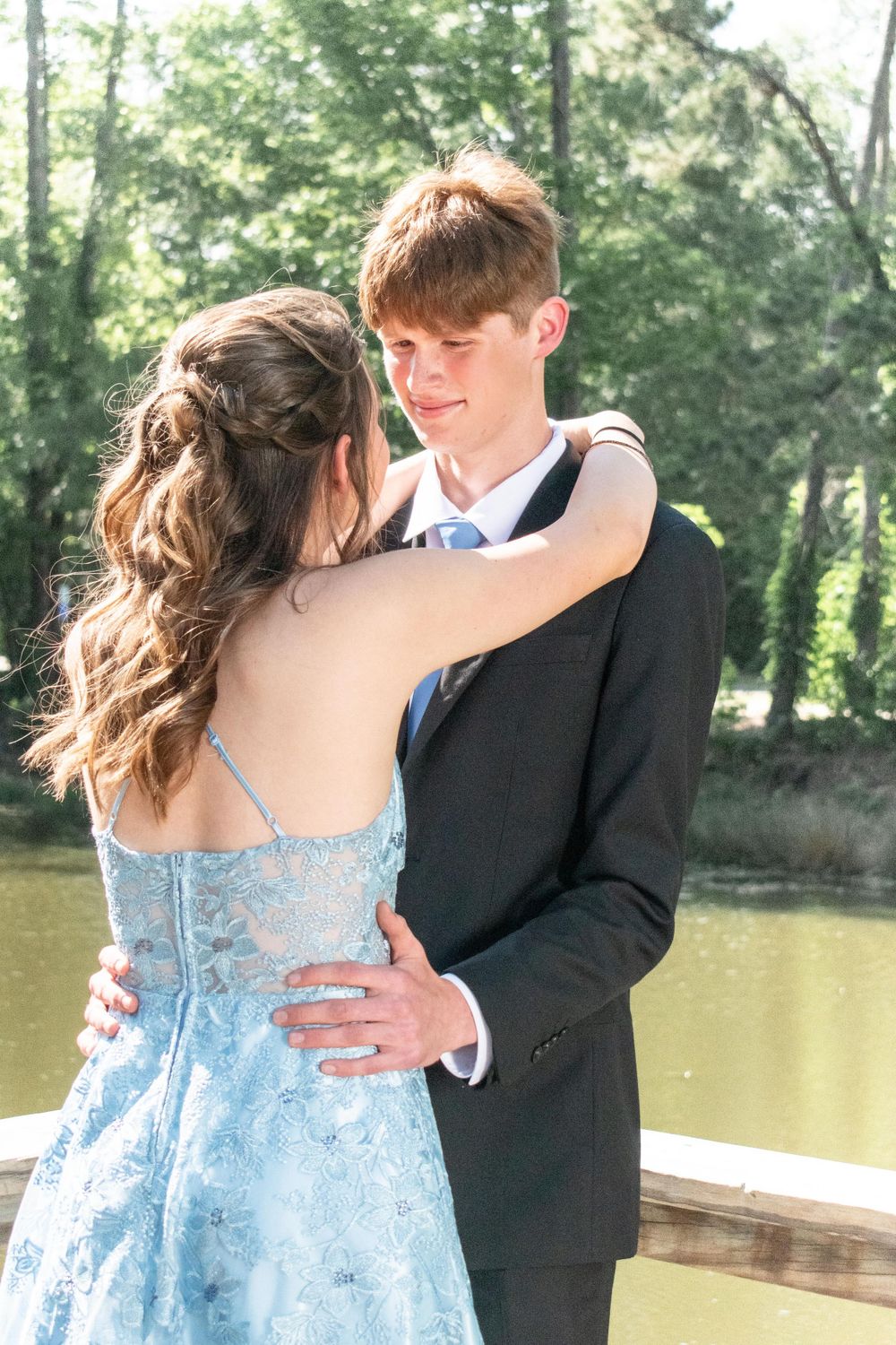 Romantic moment captured between couple in formal wear by lakeside deck.