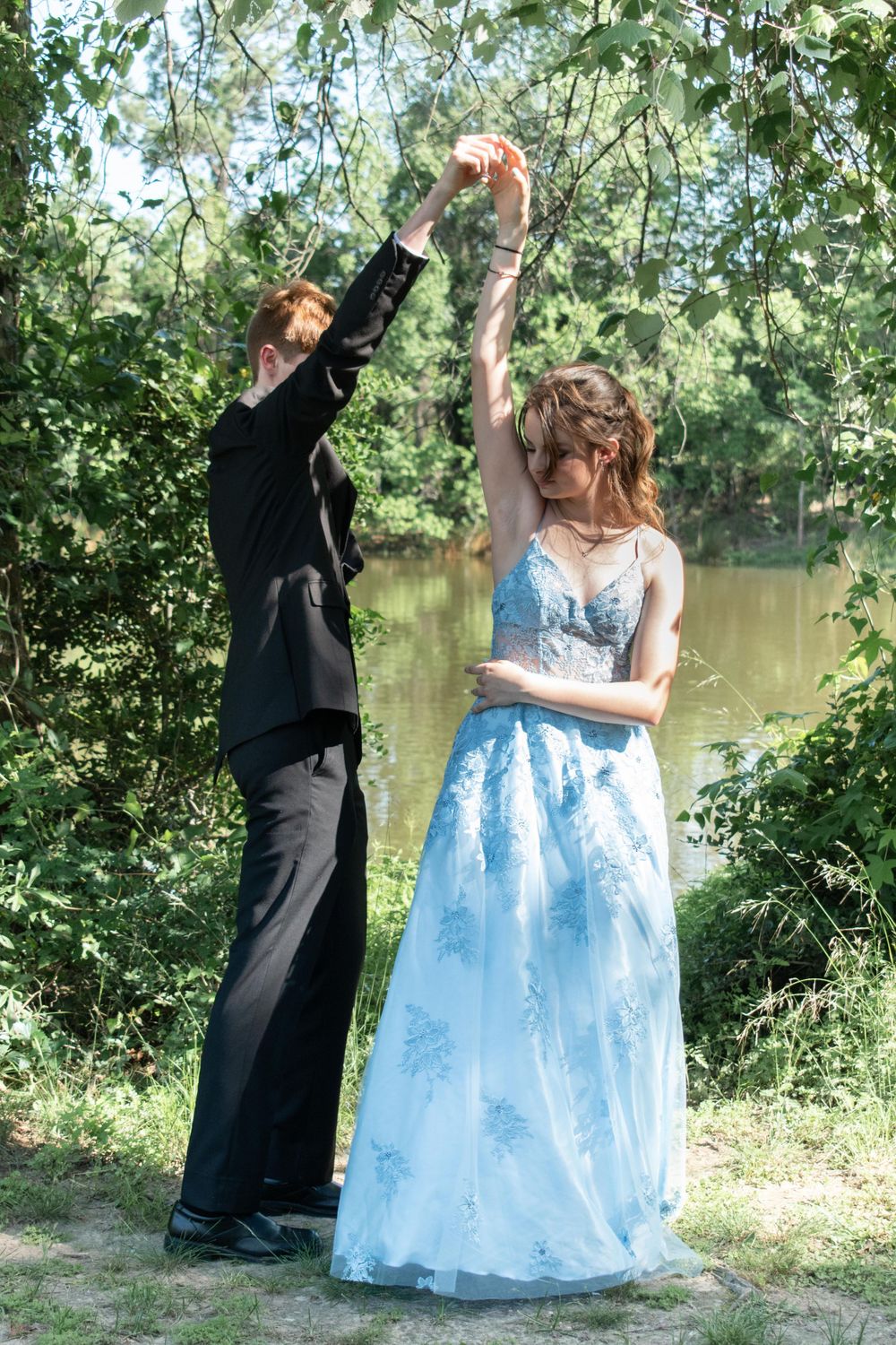 Playful dancing moment between couple in formal wear by scenic pond.