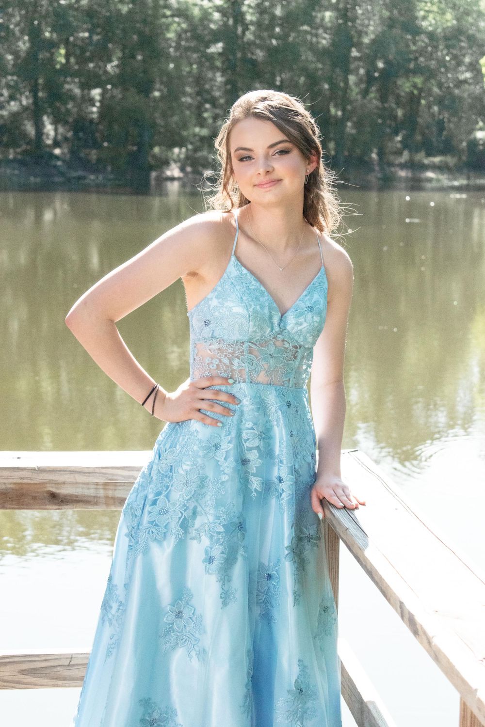 A light blue prom dress with lace detail shimmers as its wearer poses by a lake.