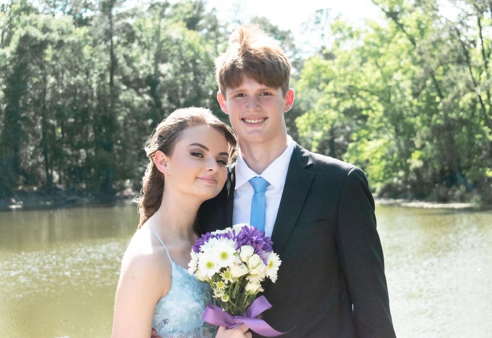 Formal portrait of couple by pond with purple bouquet and light blue gown.