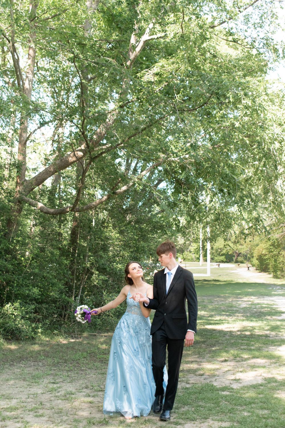 Couple walking together on nature path wearing blue gown and black suit.