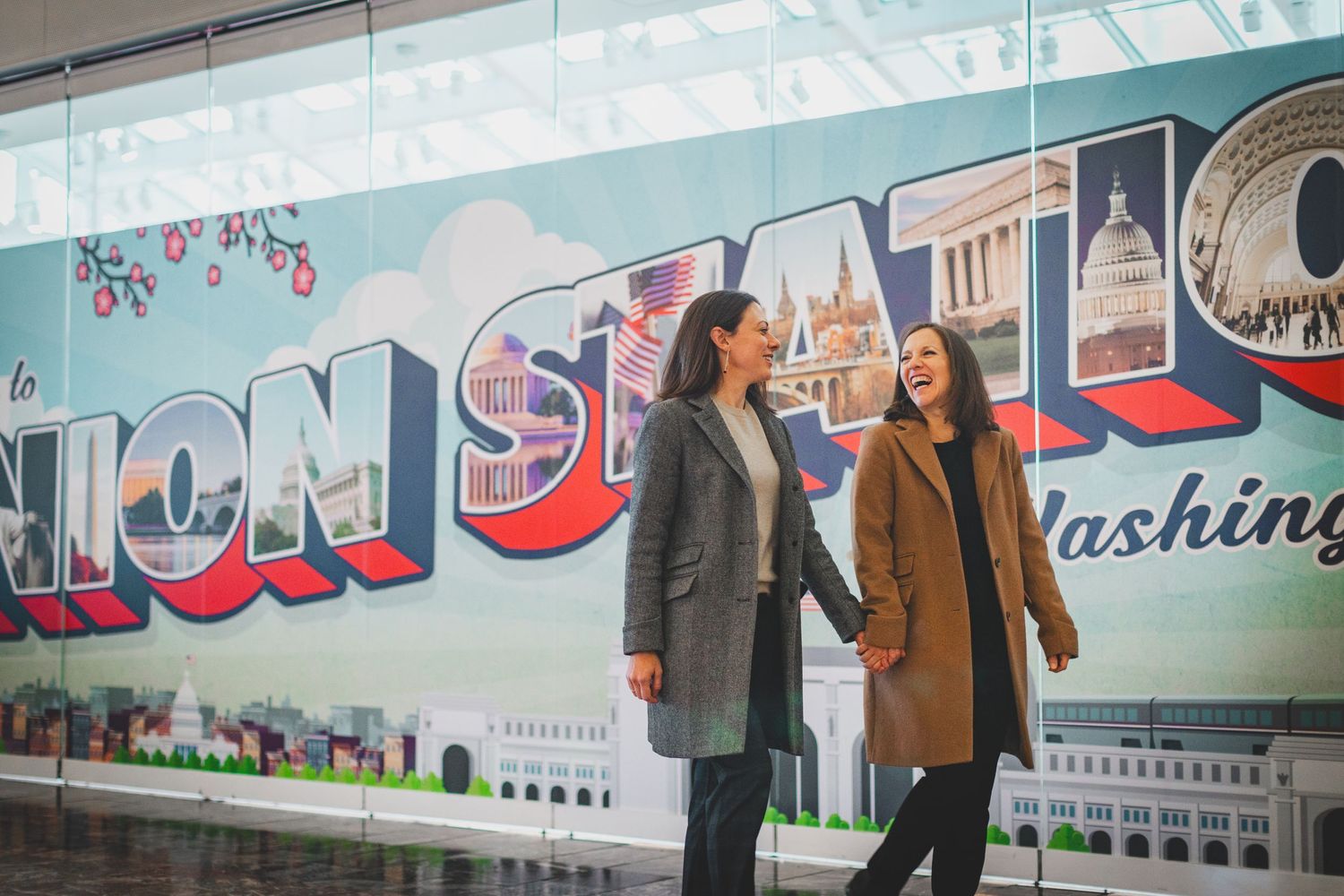 Two people stand in front of a colorful Washington DC mural in winter coats.