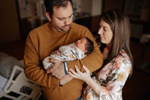 New parents in hospital room tenderly holding their swaddled newborn baby.