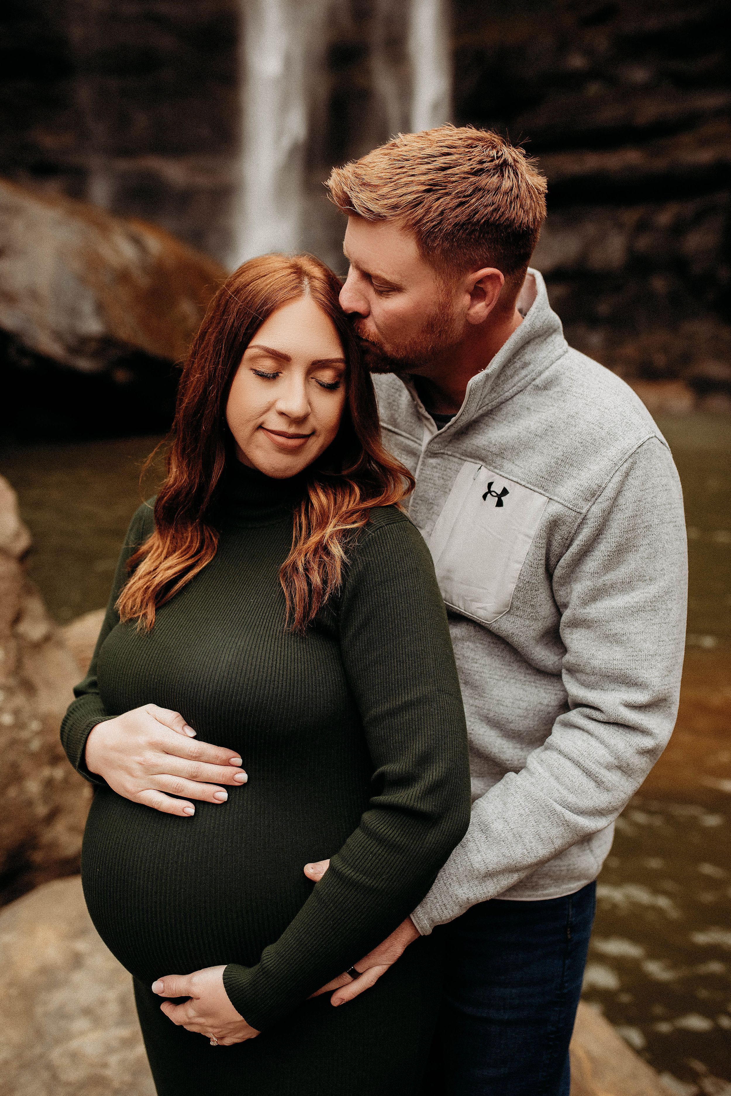 Couple sharing tender moment with waterfall backdrop during maternity session.