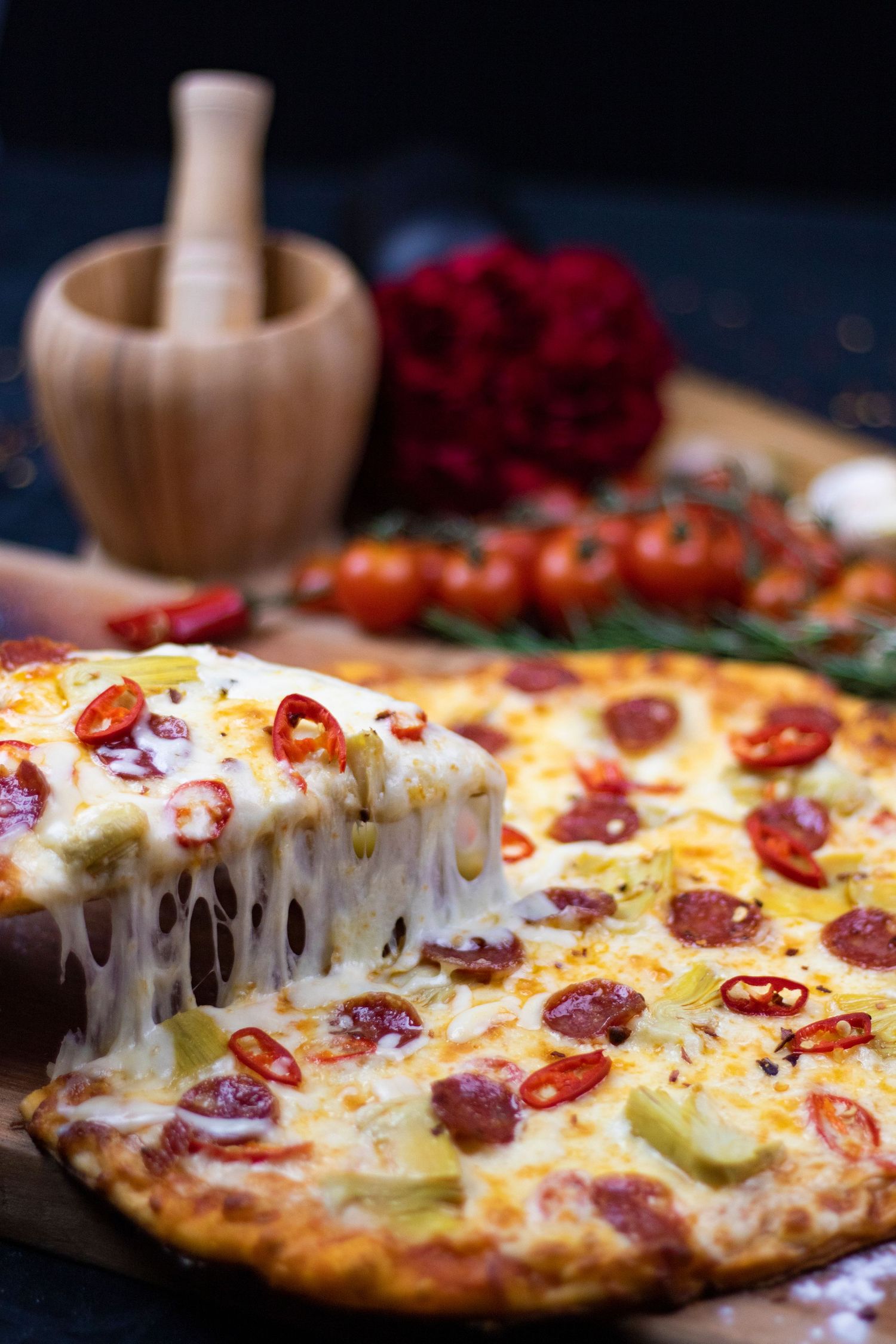 Close-up of melty cheese pizza with pepperoni and chili peppers on dark background.