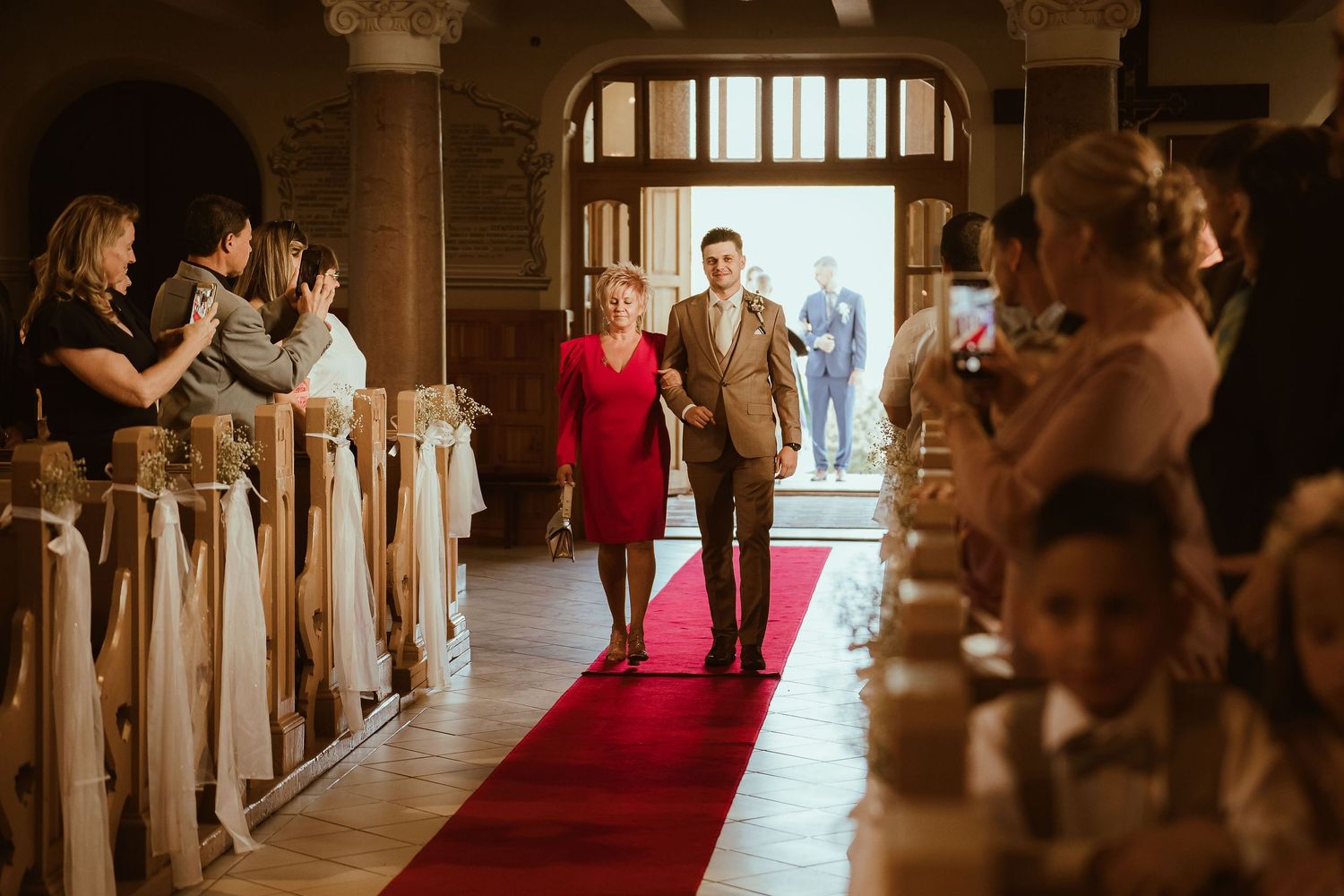 Wedding guests line the church pews as attendants walk down a red-carpeted aisle.