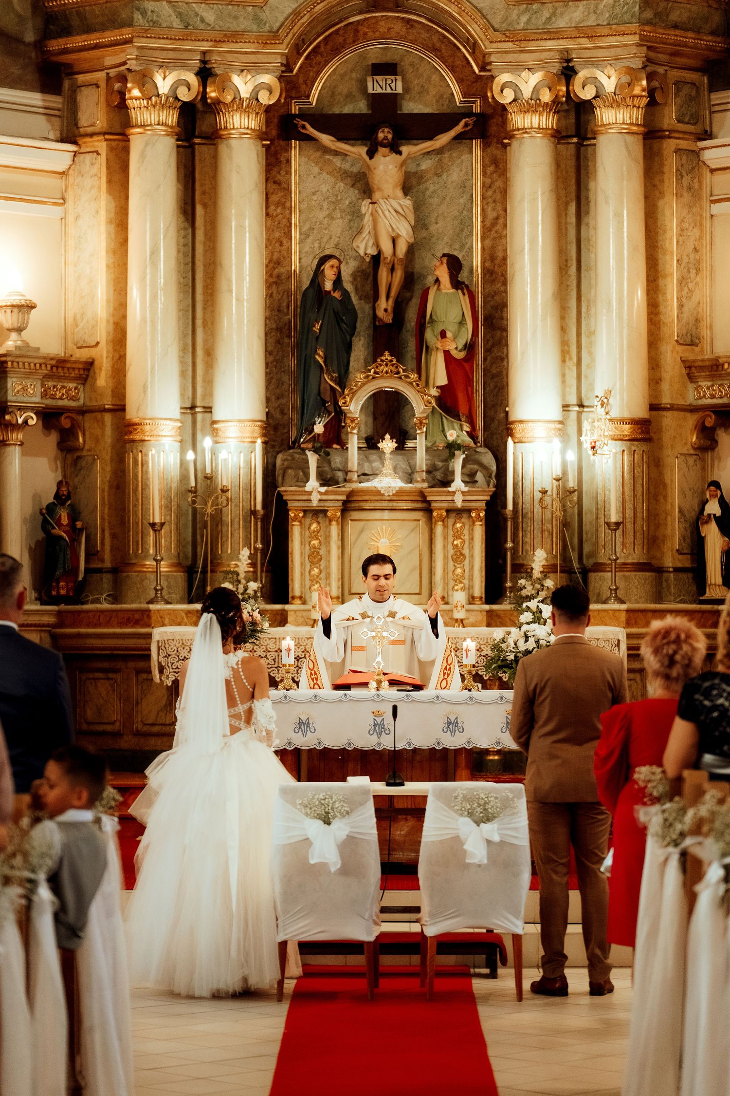 A wedding mass taking place in a grand cathedral with elaborate golden altar and religious artwork.