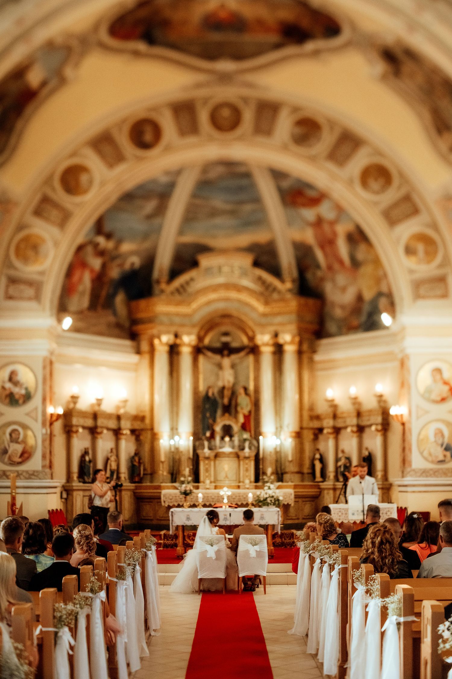 Interior of a Catholic church with baroque architecture and painted dome during a wedding ceremony.