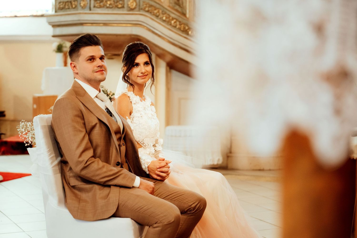 A wedding couple seated during their ceremony in an ornate church sanctuary.
