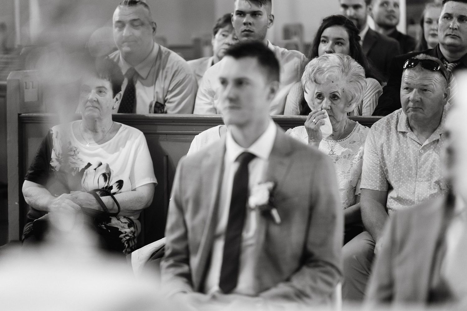 Black and white photo of guests watching attentively during a formal church ceremony.