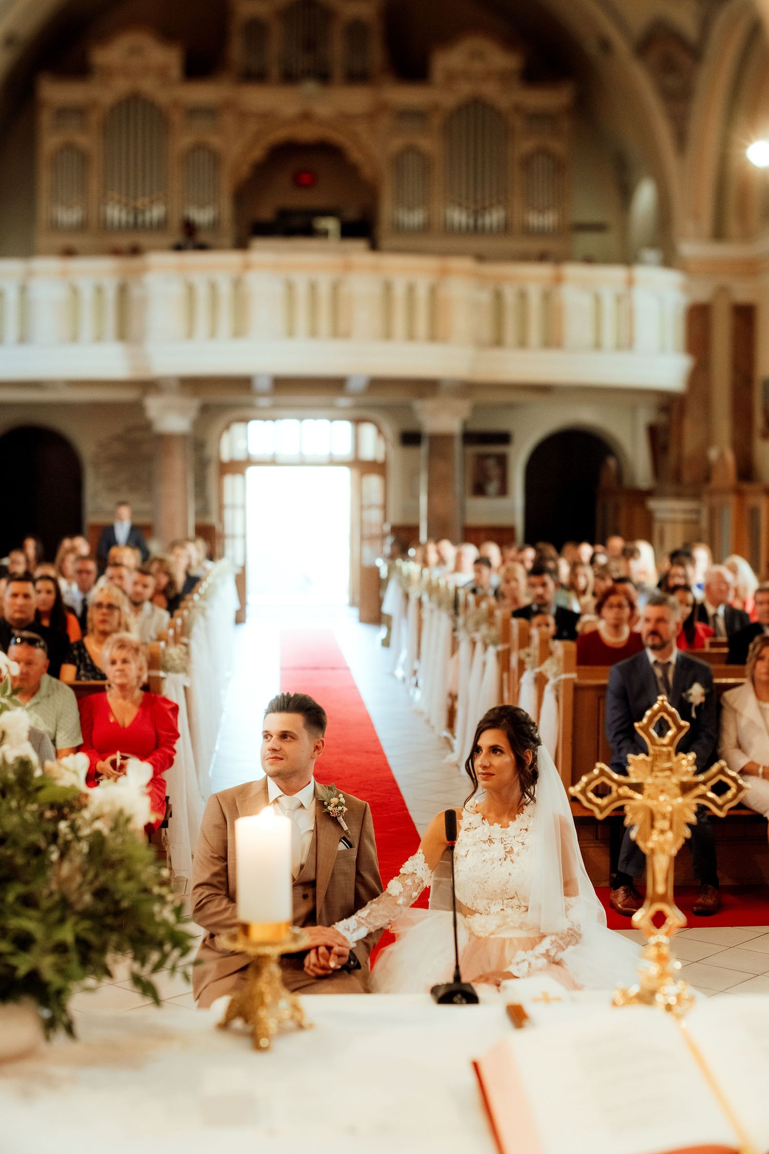 Wedding couple seated at altar during Catholic ceremony with decorative gold cross.