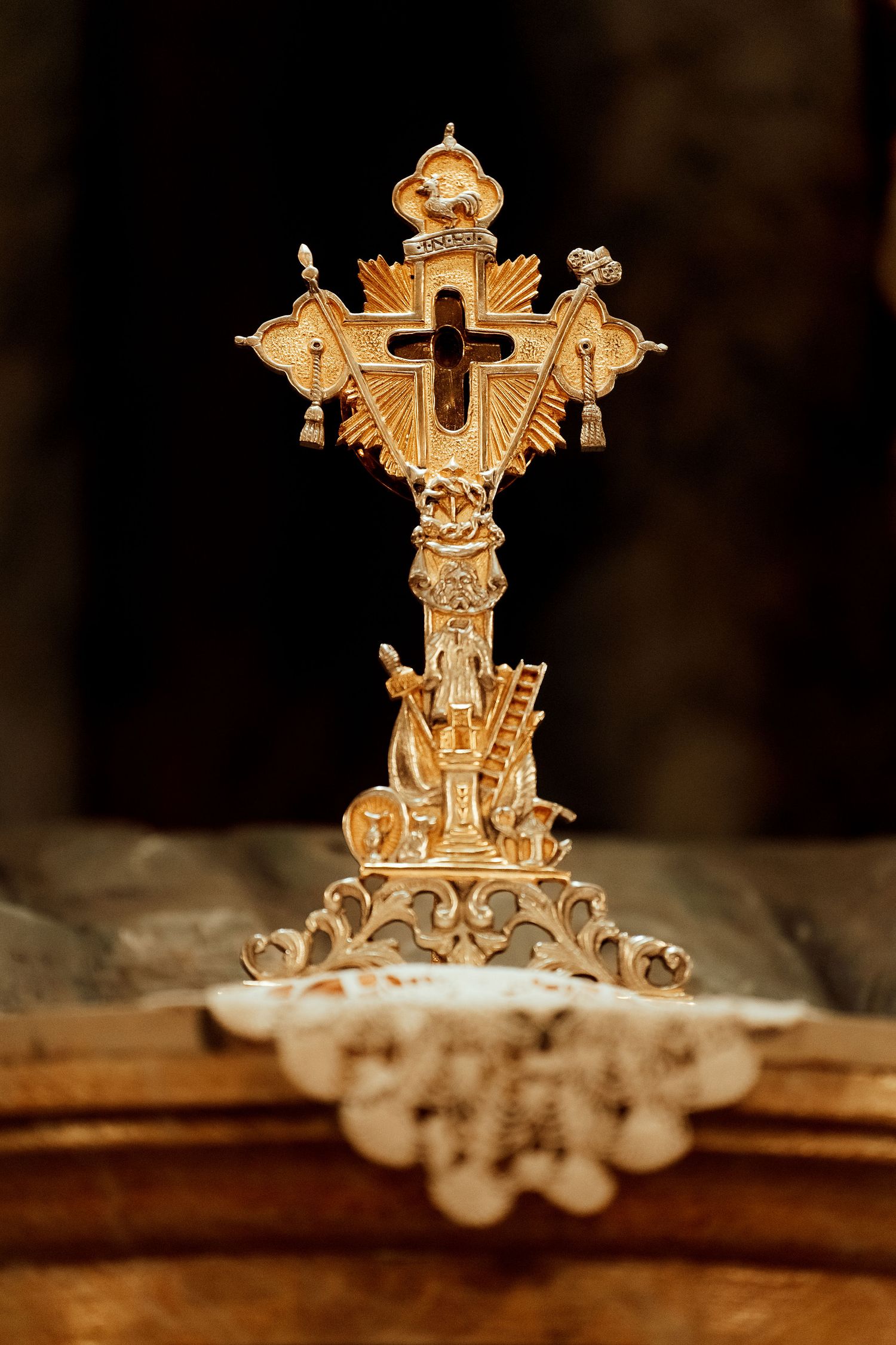 Ornate golden Catholic cross with decorative details photographed against dark background.