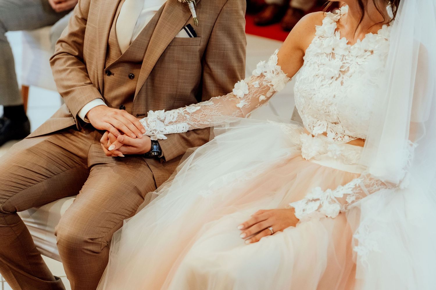 Wedding couple in brown suit and white lace dress seated during ceremony.