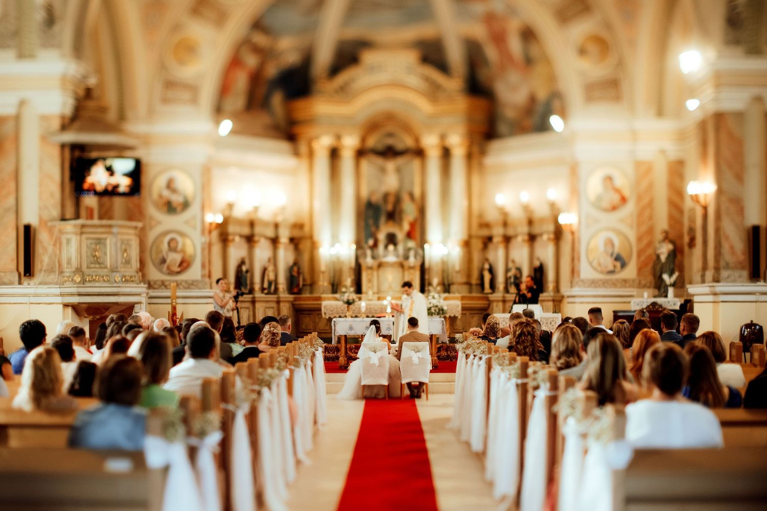 Beautiful church interior with red carpet aisle and guests during wedding ceremony.