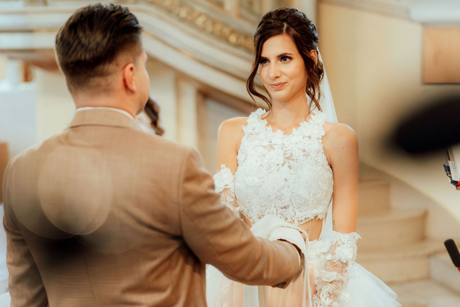 A couple shares an intimate moment during their wedding ceremony with the bride wearing a detailed lace dress.