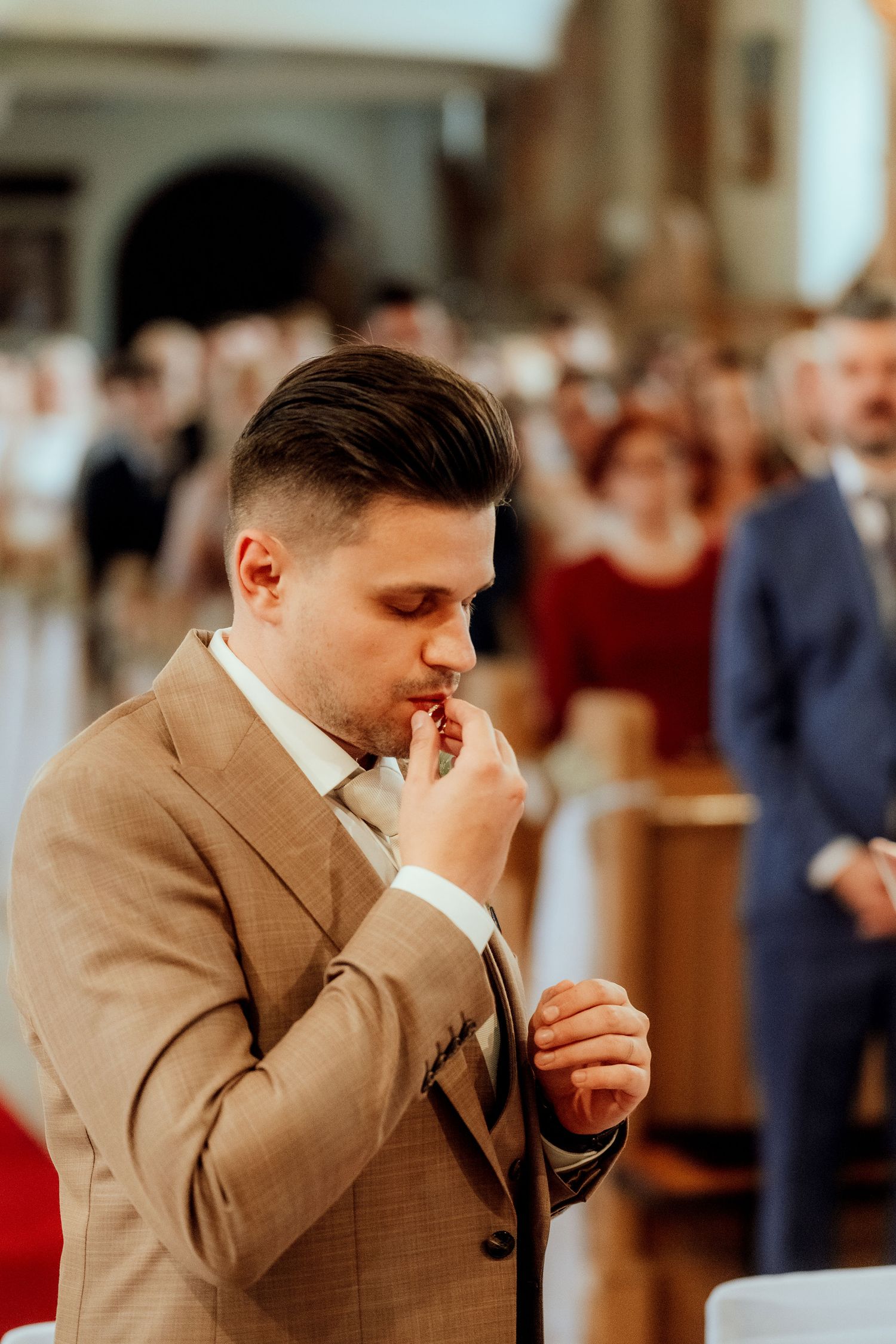 A person in a tan suit shows emotion during a wedding ceremony in a church setting.
