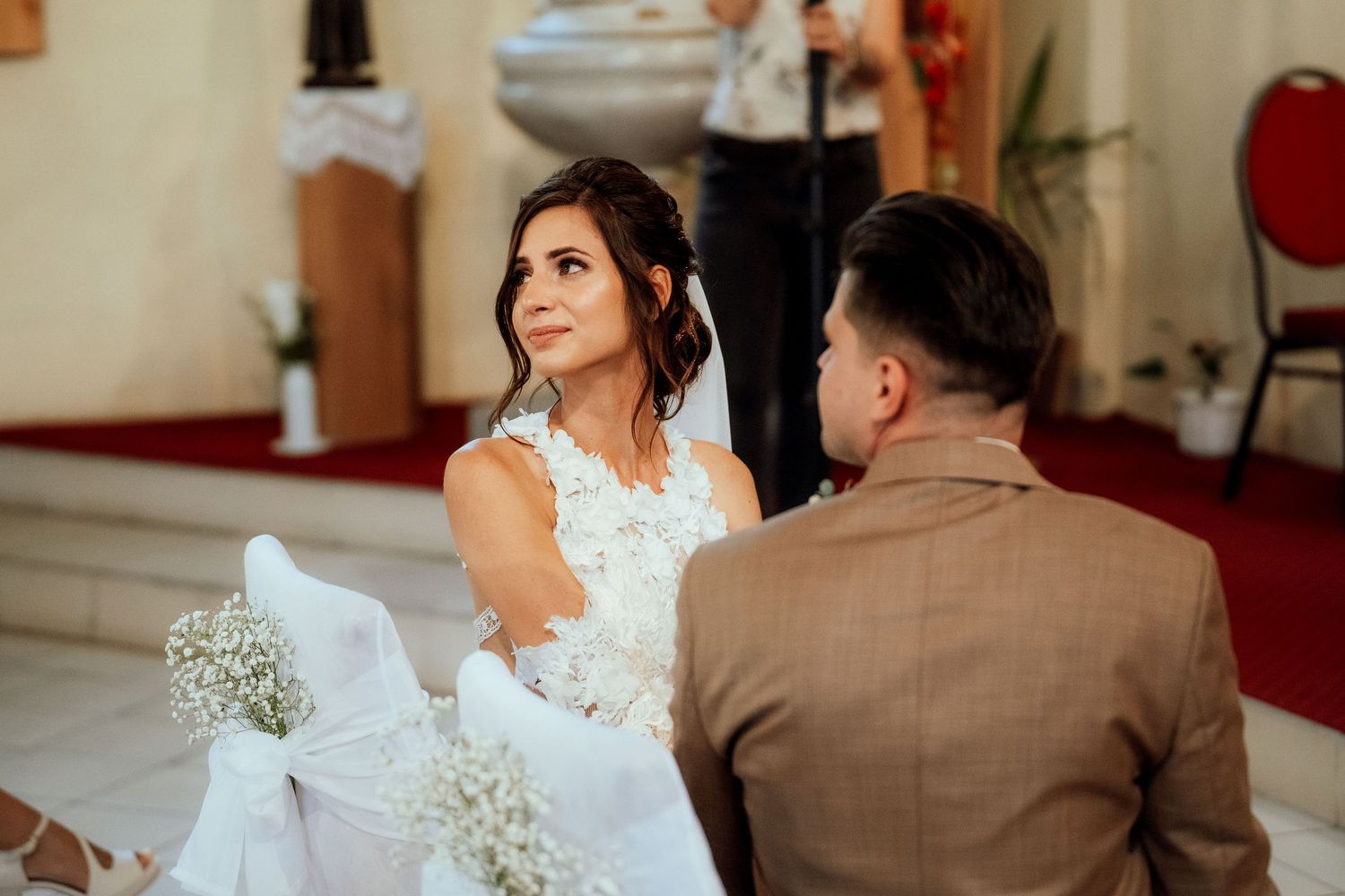 A couple during their wedding ceremony seated in an ornate church with white baby's breath floral decorations.