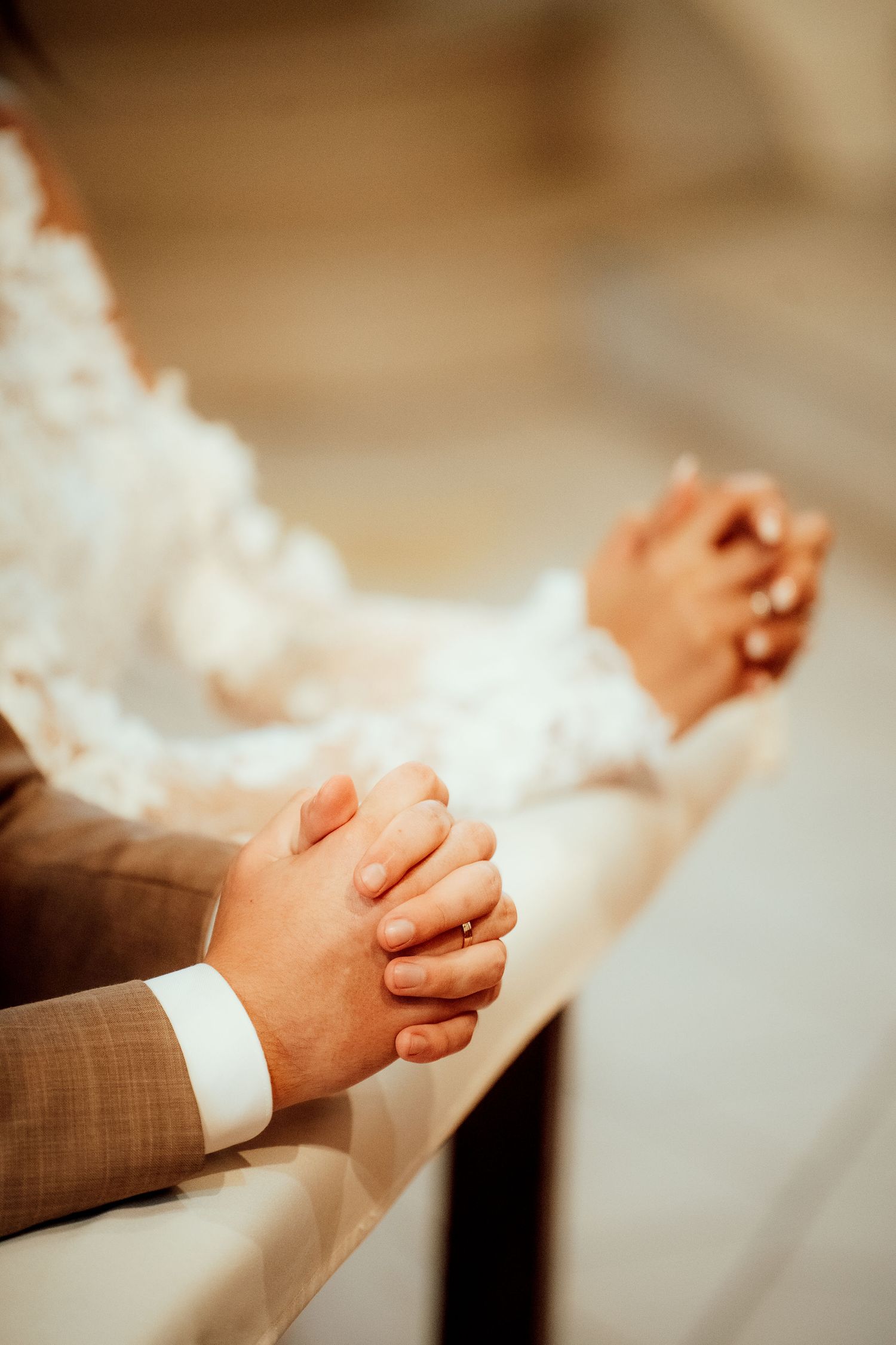 Folded hands in prayer during a wedding ceremony with a white dress and brown suit visible.