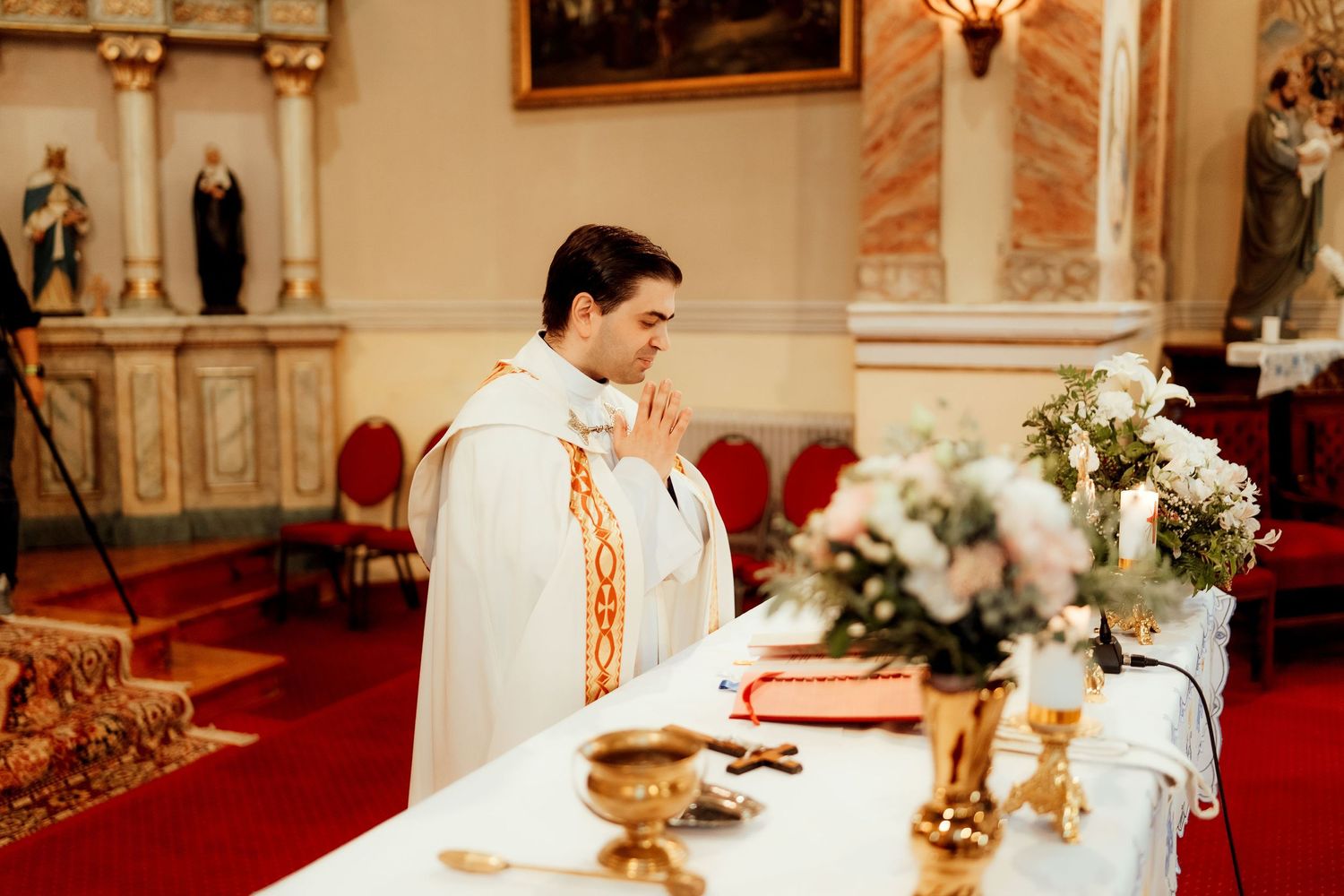 Priest performing religious ceremony at ornate church altar with golden chalice.