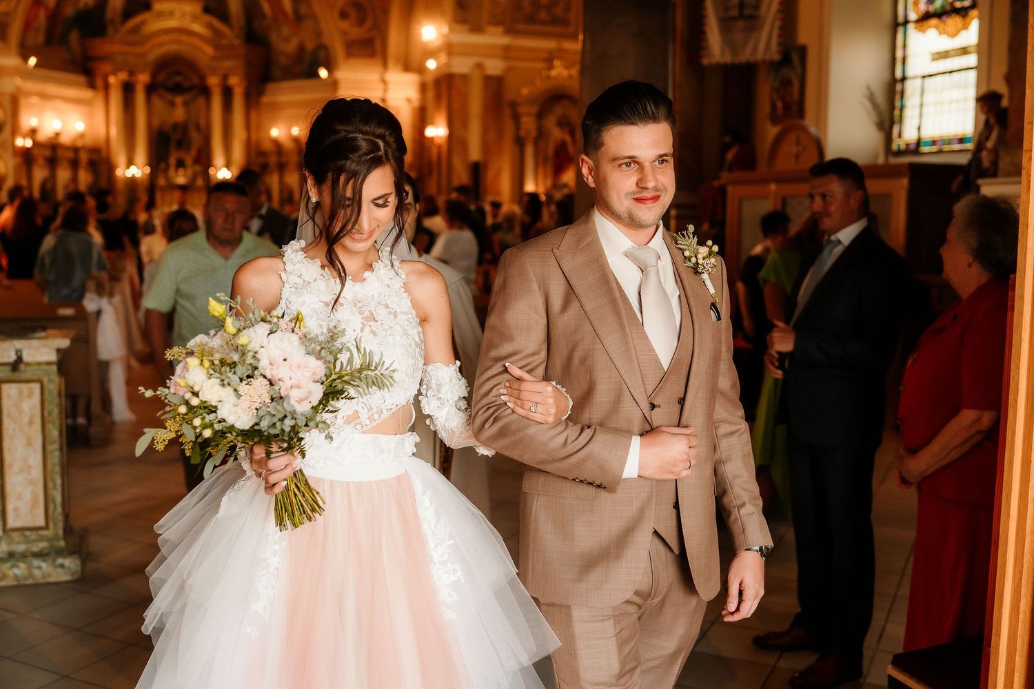 Couple walking together in an ornate church with tan suit and white wedding dress.
