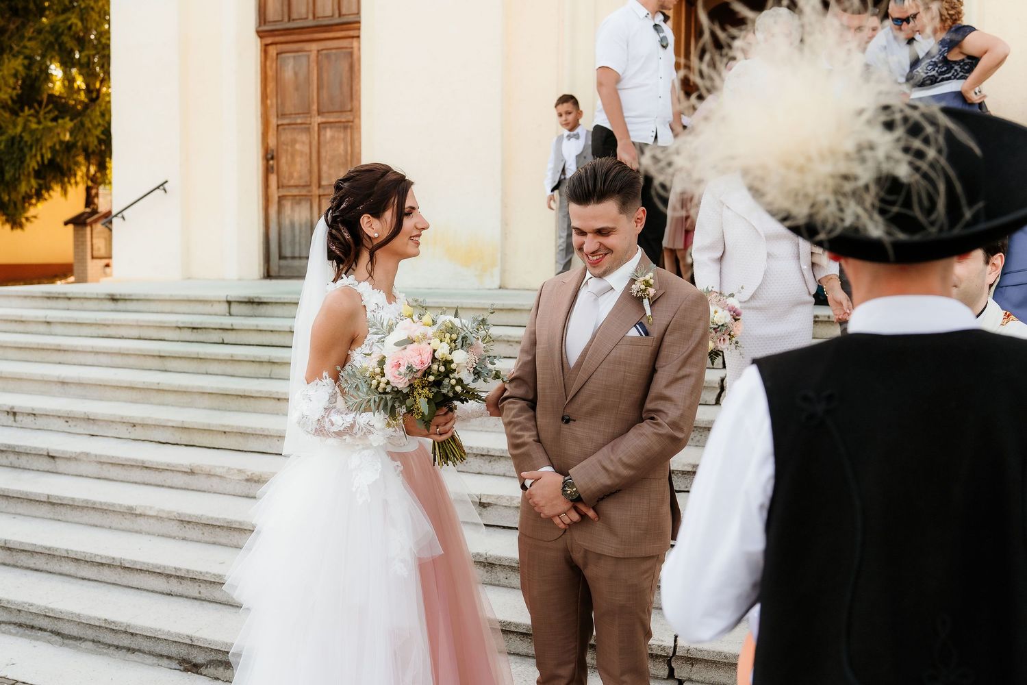 Outdoor wedding ceremony on church steps with soft pink floral bouquet.