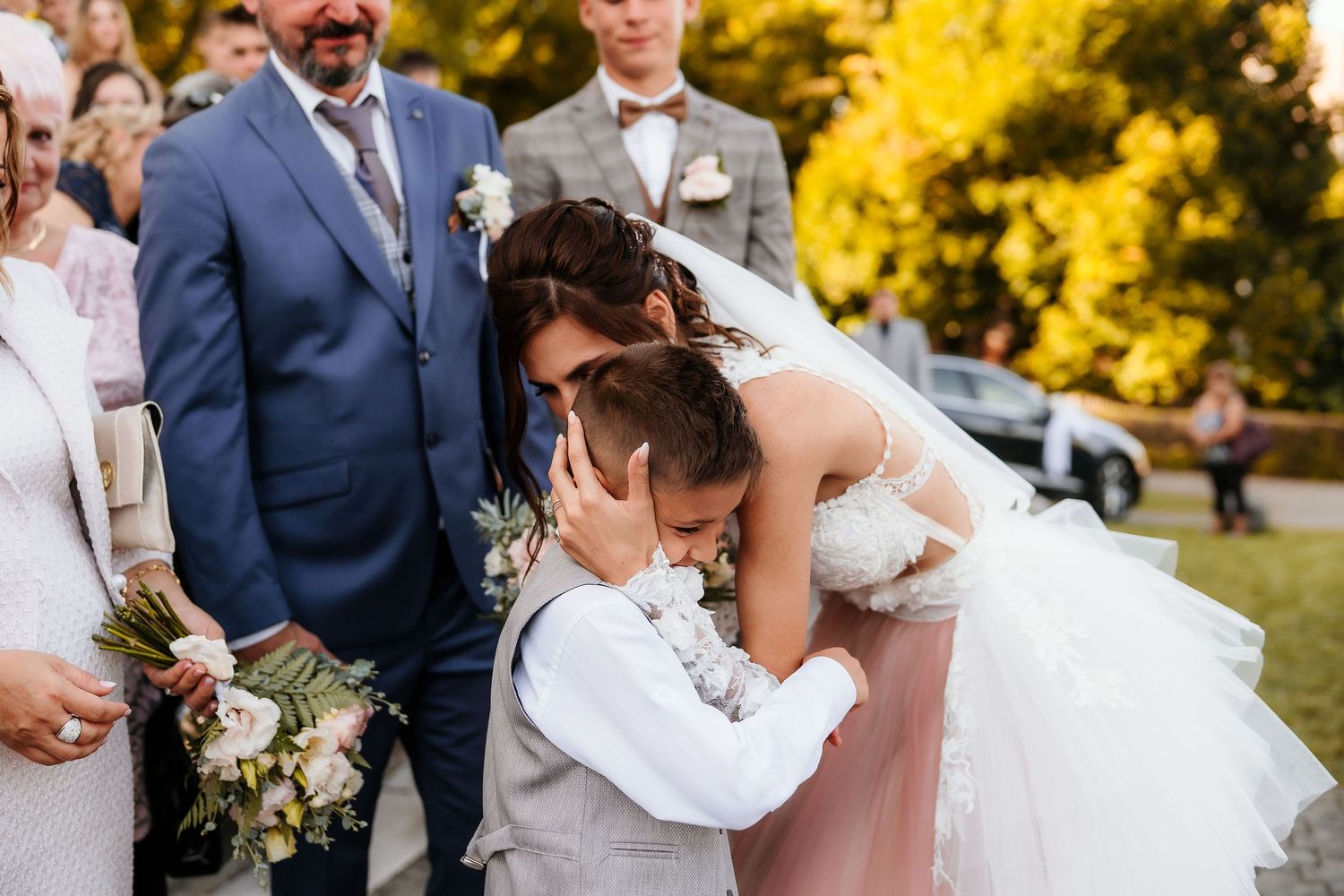 A tender moment during an outdoor wedding ceremony with autumn foliage in the background.