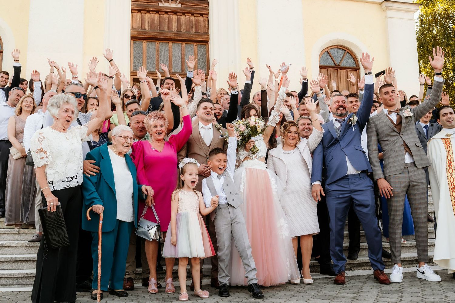 Joyful wedding guests raising their hands and celebrating on church steps.