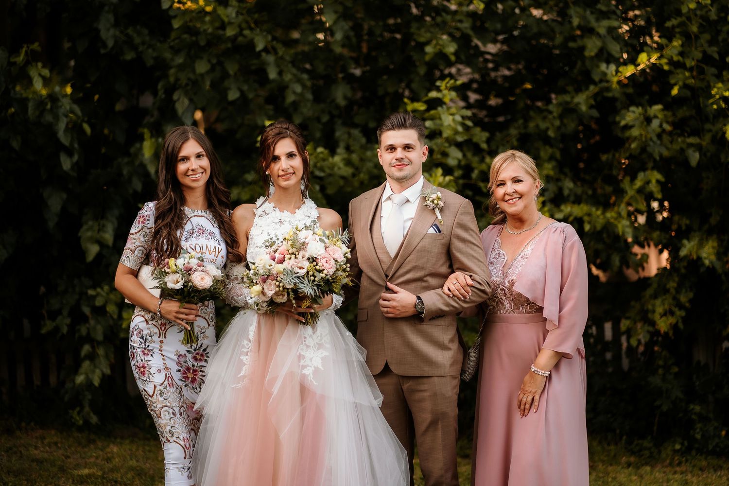 Bridal party poses together outdoors wearing formal attire in pink and neutral tones.