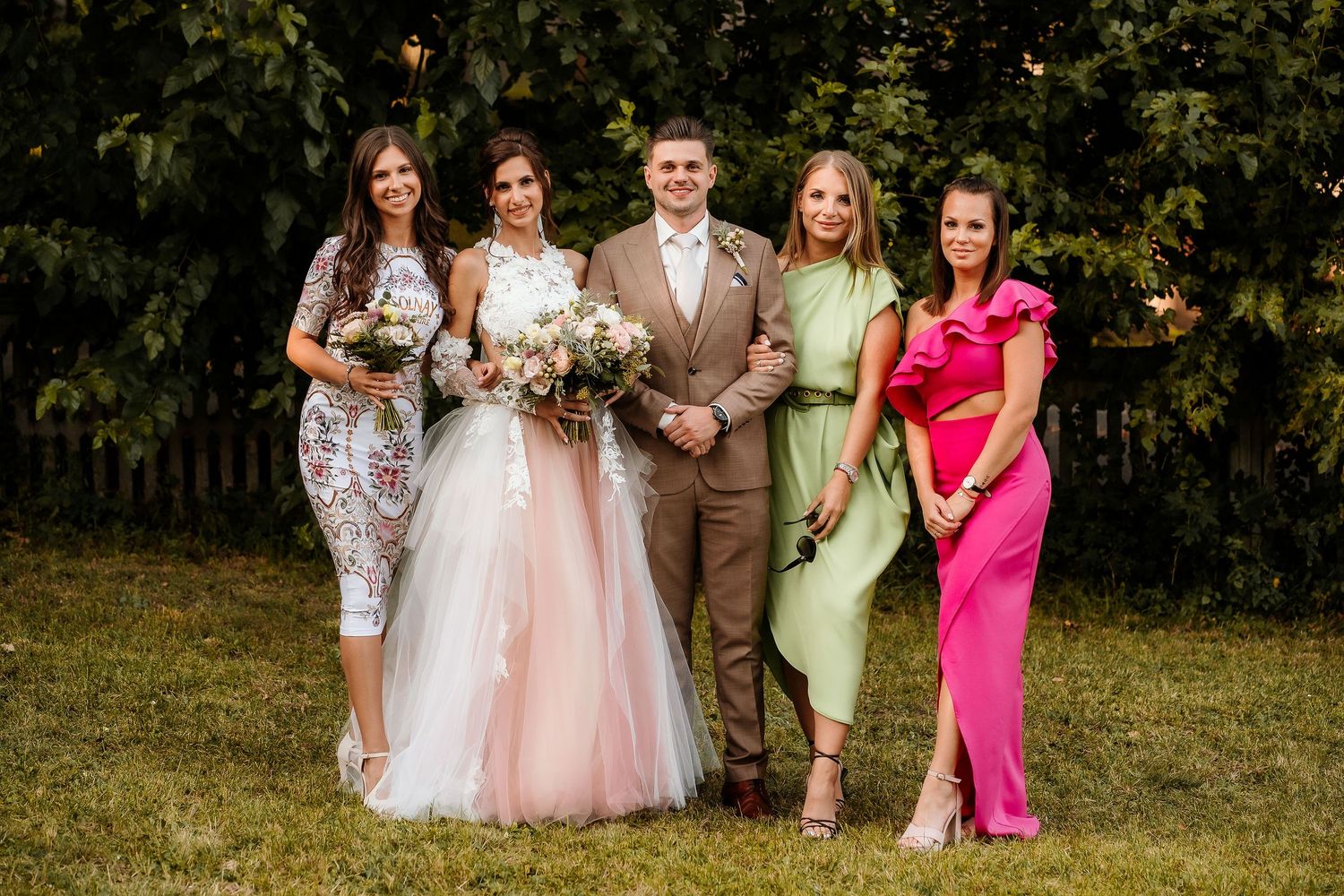 Wedding party members pose in coordinated formal attire with pink and floral dresses.