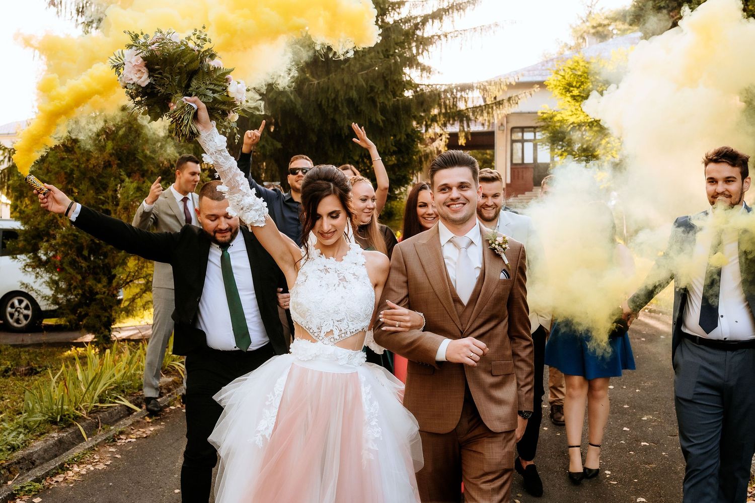Couple celebrates with yellow smoke bombs during outdoor wedding festivities.