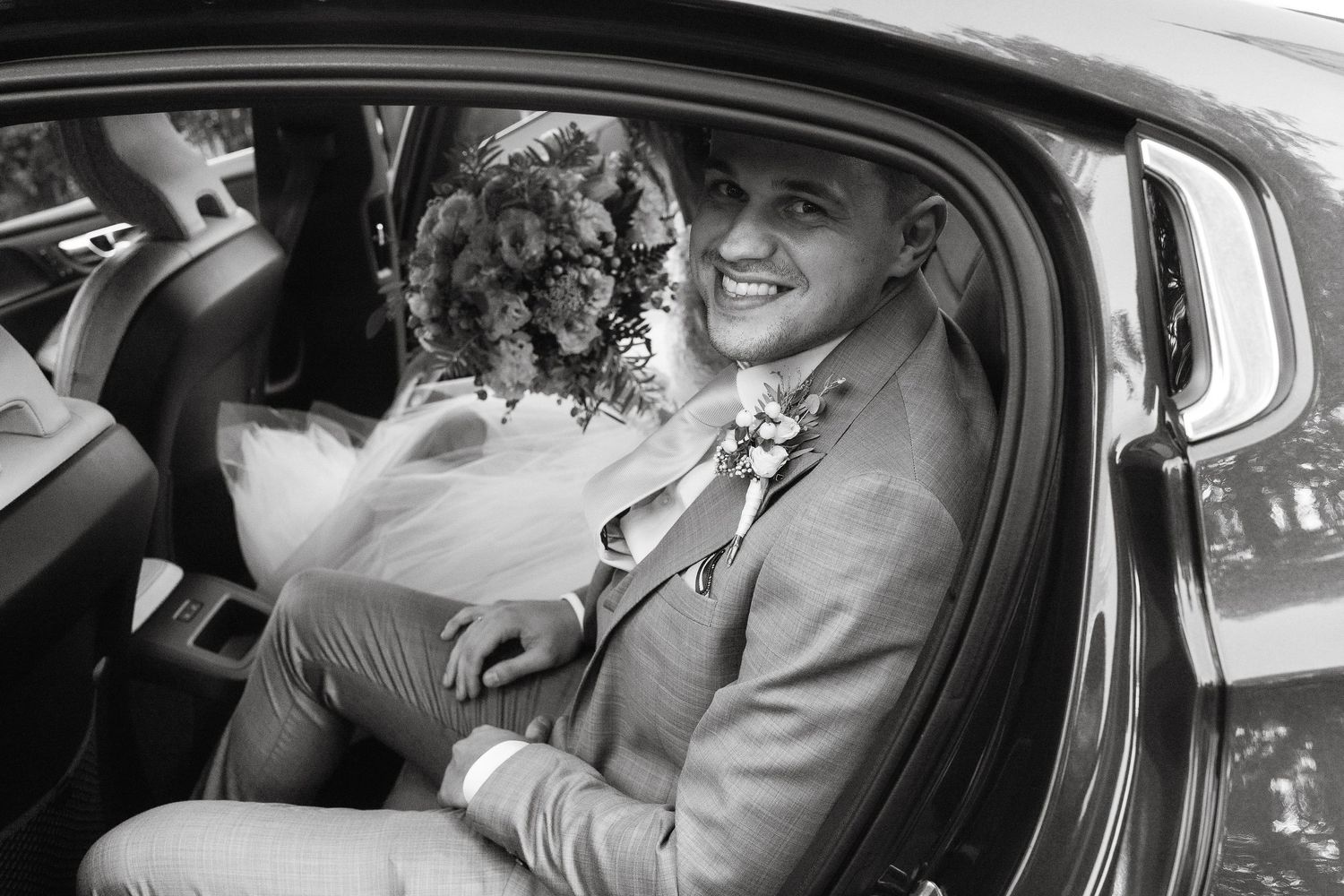 Black and white candid photo of wedding couple sharing joyful moment in car.