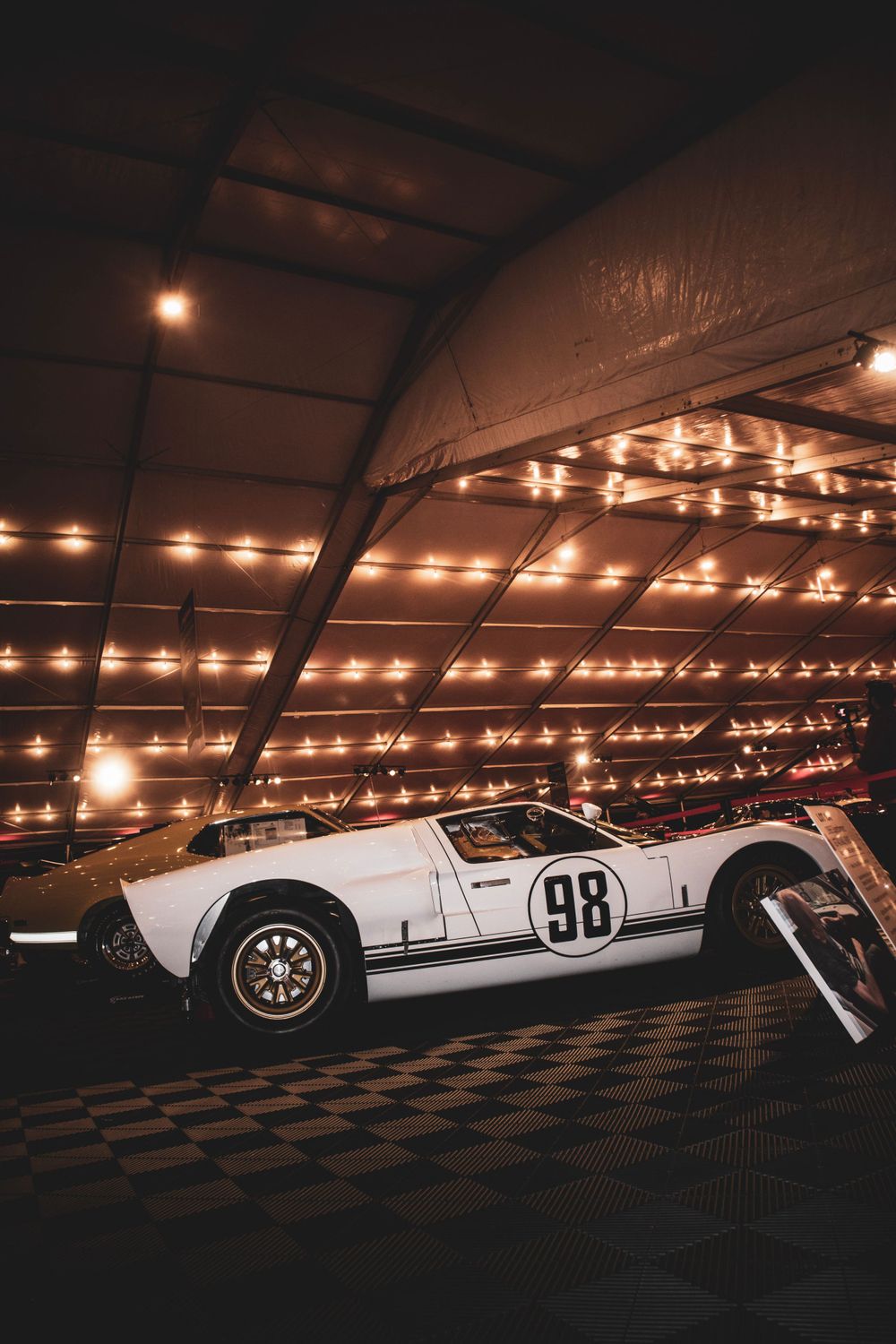 White vintage race car number 98 illuminated by decorative string lights in an exhibition space.