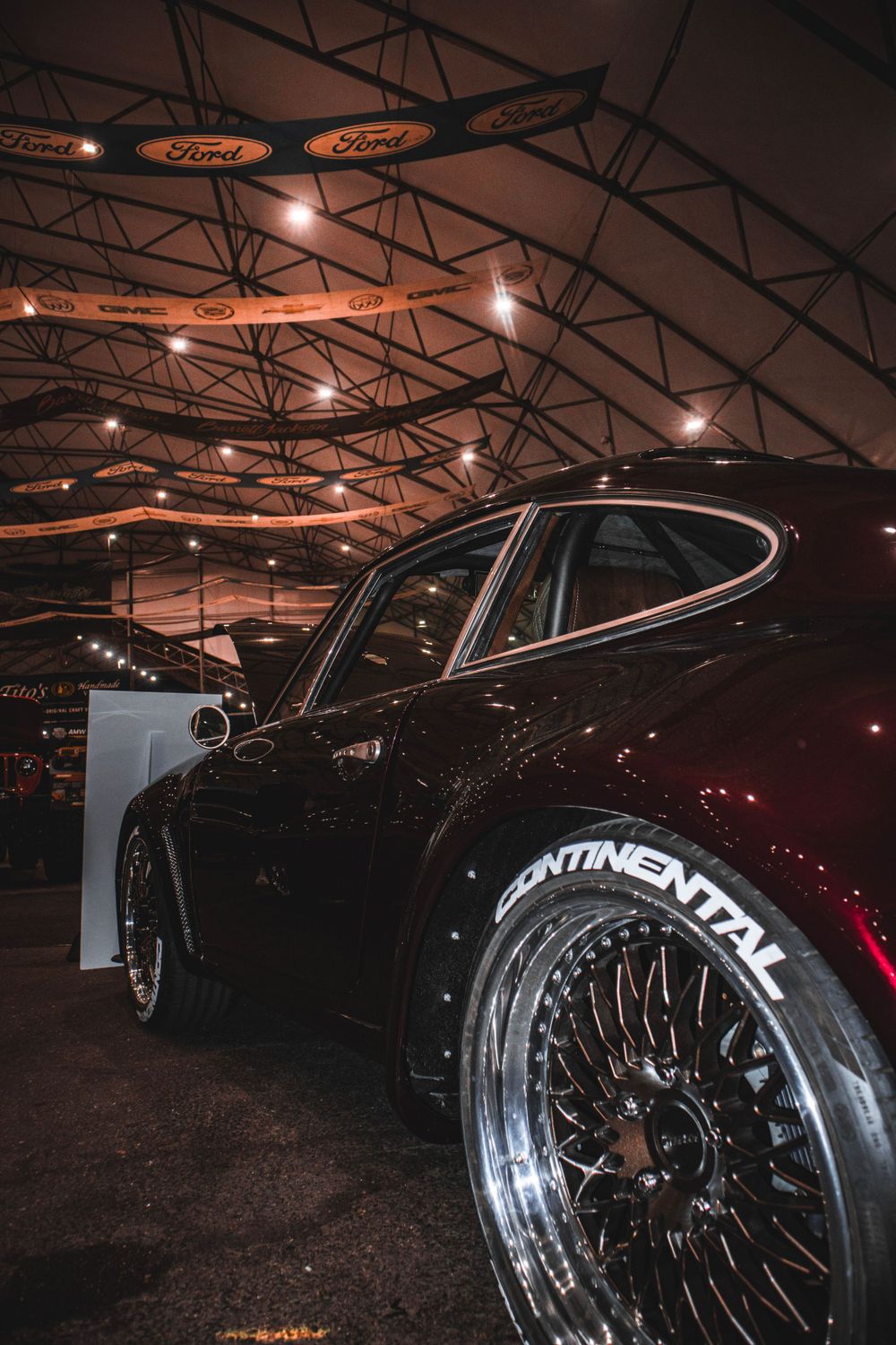 Modified Porsche with custom Continental wheels photographed at indoor car show with dramatic lighting.