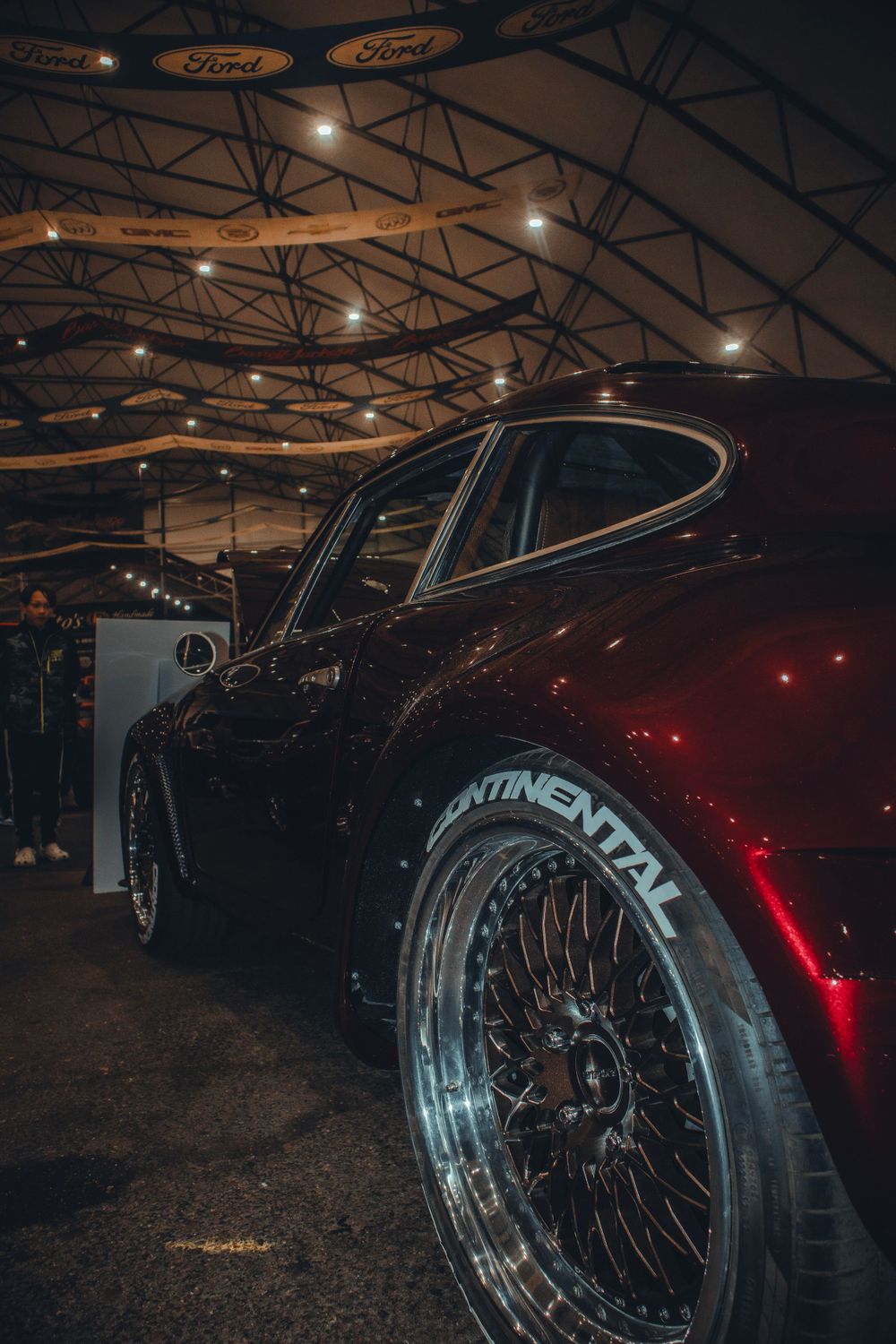 Black Porsche with Continental tires and custom wheels under industrial venue lighting.