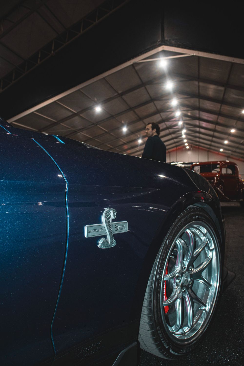 Close-up of a dark blue performance car's fender and wheel at a nighttime car show.