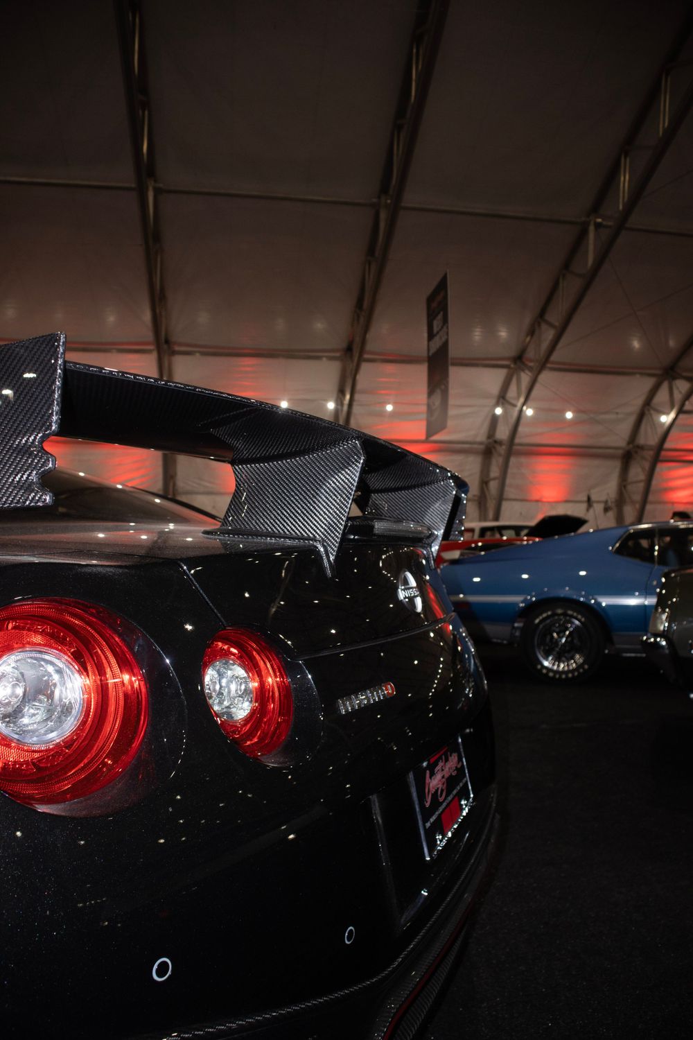 Black Nissan GT-R rear wing and taillights under dramatic indoor lighting.