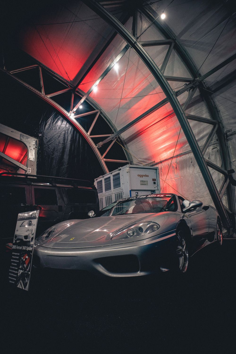 Silver Ferrari under red-lit architectural structure at indoor auto show.