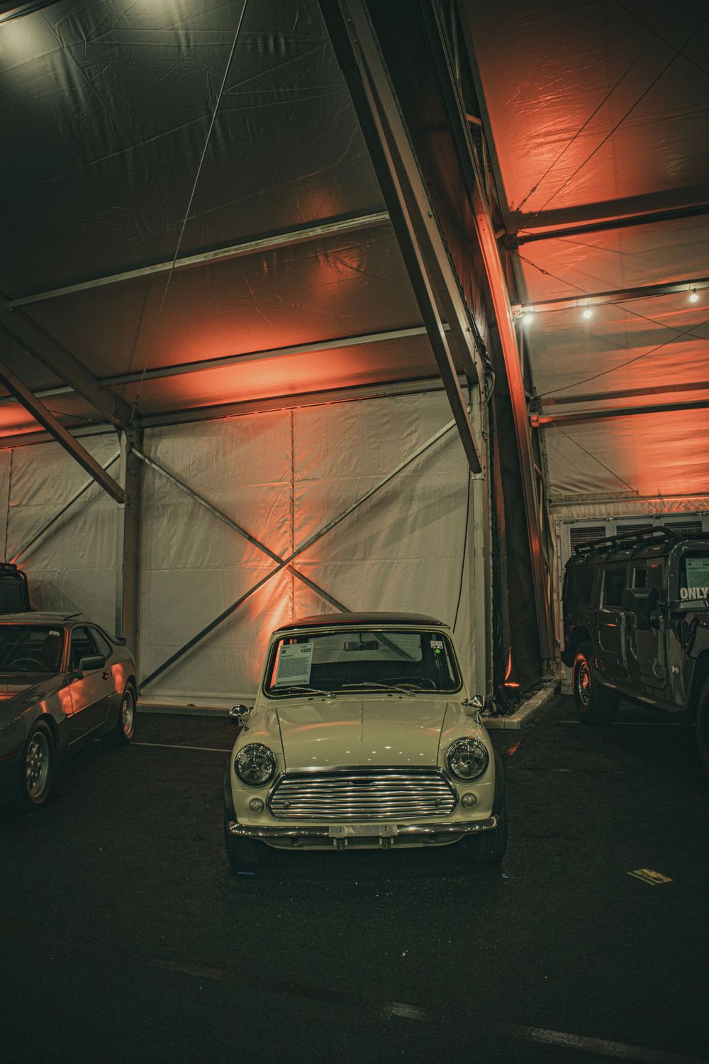 Classic Mini Cooper displayed in a dimly lit indoor space with orange-tinted lighting and industrial ceiling.