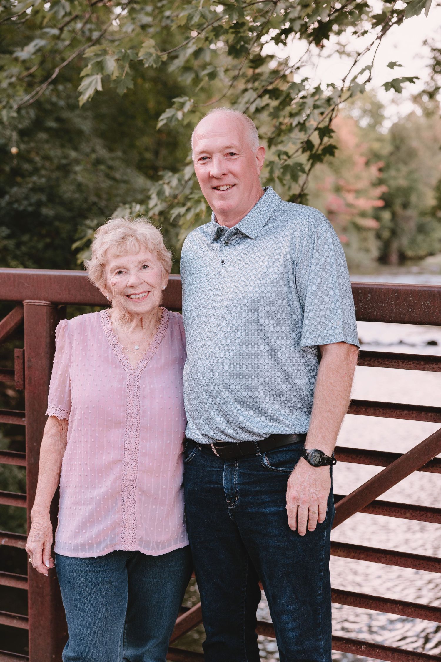 Two people standing together on wooden deck with trees in background.