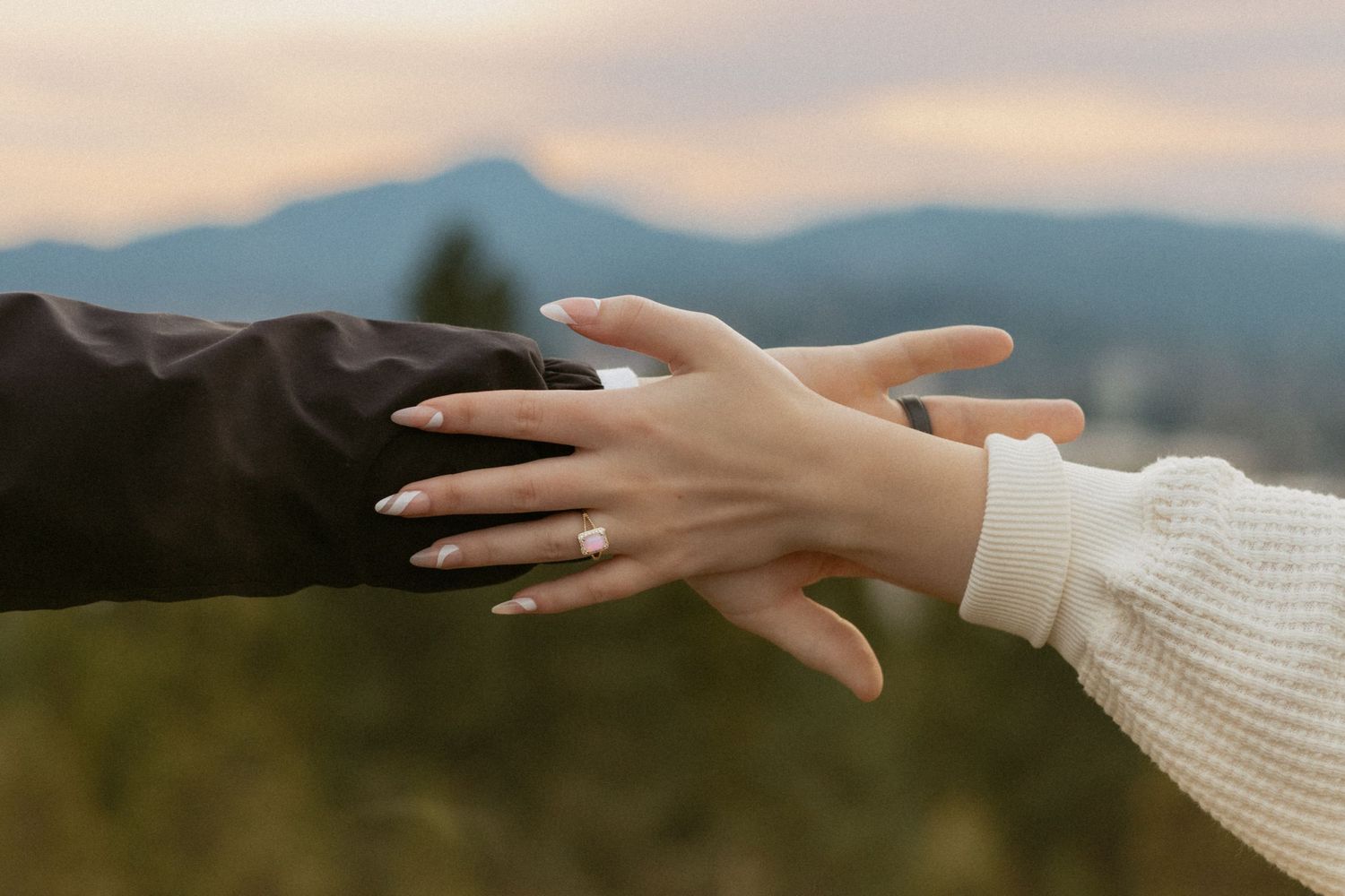 Hands reach towards each other against a sunset mountain backdrop.