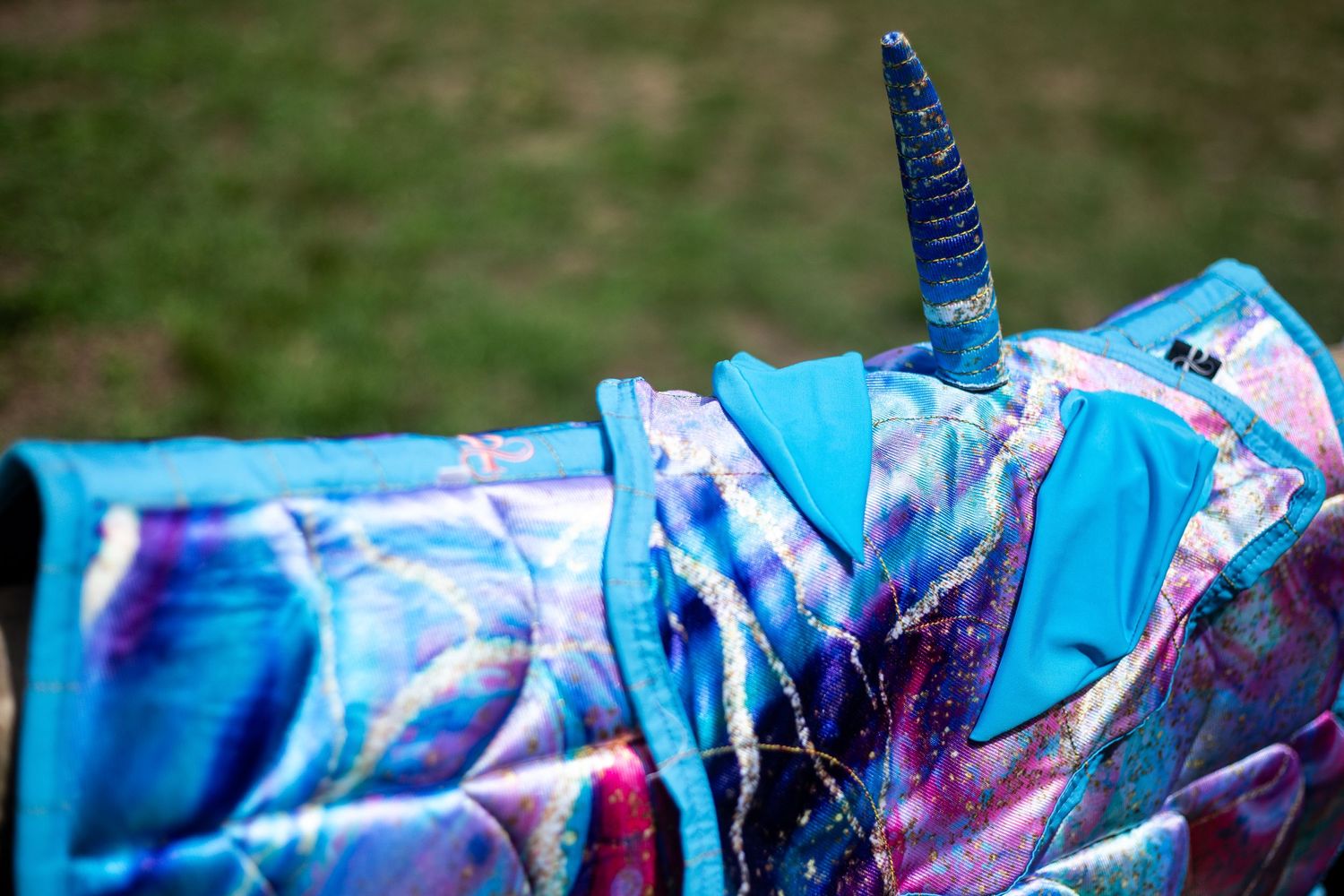 Close-up of a colorful blue iridescent unicorn costume with a spiral horn on a horse blanket.