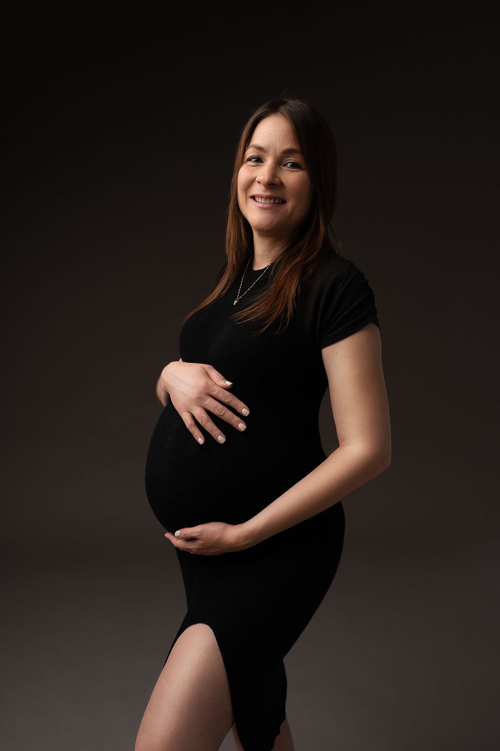 Artistic maternity portrait against dark background in black dress.