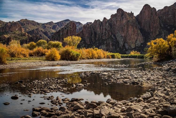 Rocky mountain landscape with autumn foliage and river flowing through rugged canyon terrain.