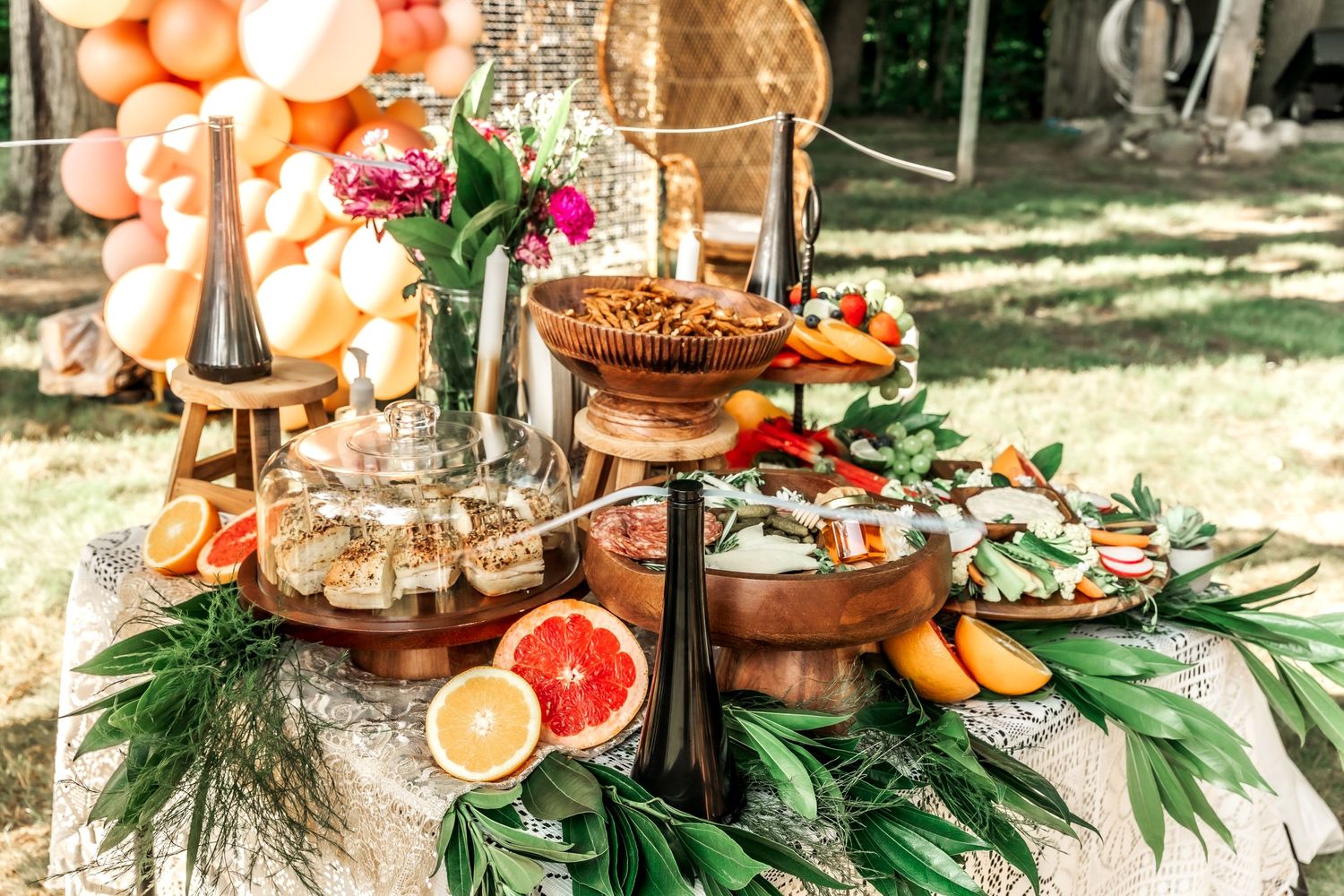Tropical-themed food display with citrus, greenery, and tiered appetizers on lace tablecloth.