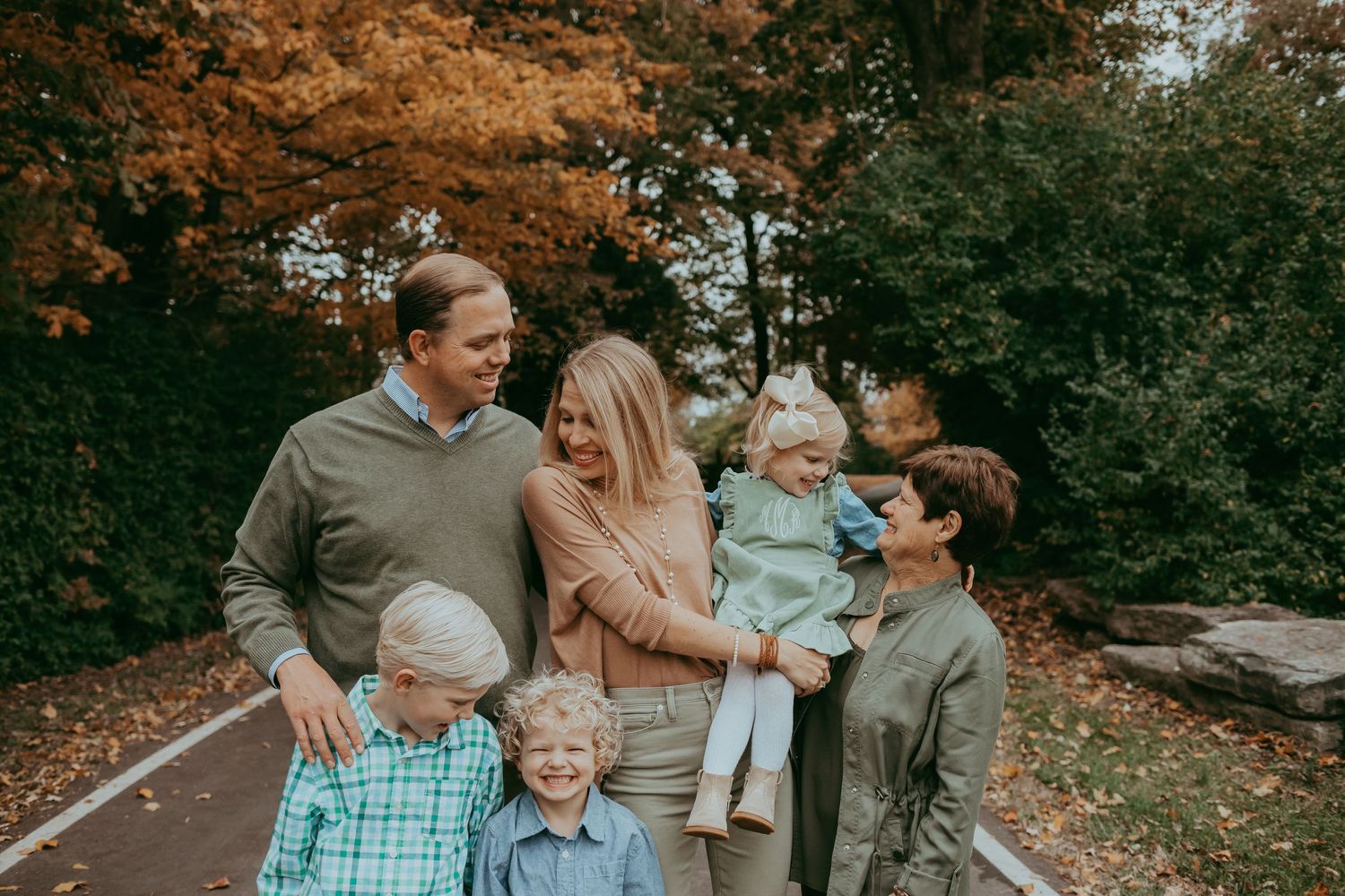 A group wearing coordinated casual outfits poses together outdoors during autumn with fall foliage in the background.