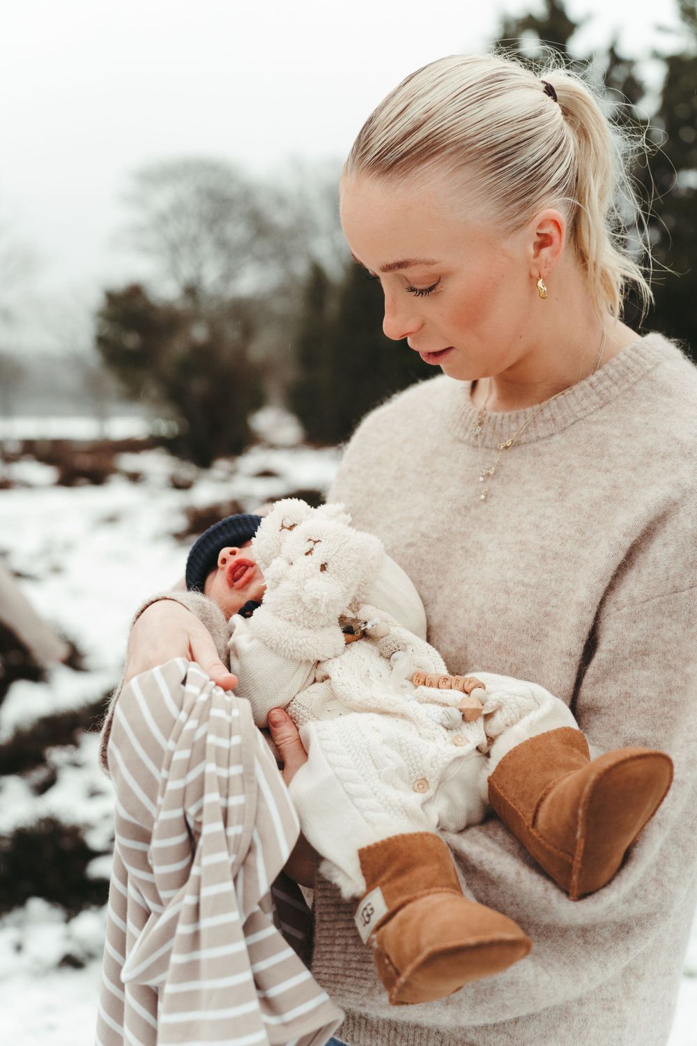 Person in beige sweater holding small items against snowy winter backdrop.