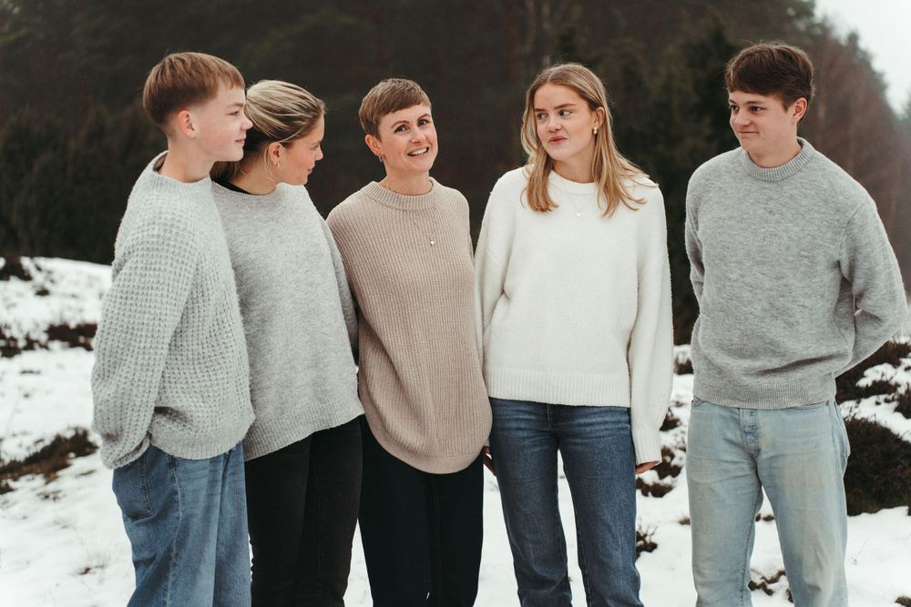 A group wearing coordinated neutral sweaters poses together in a winter setting.