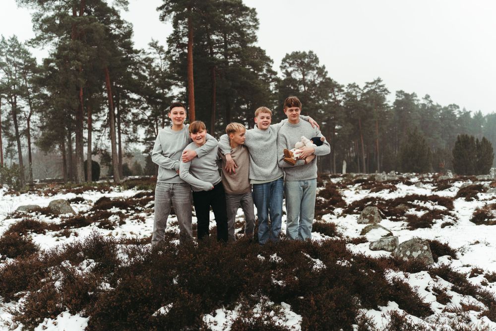 Casual group photo taken outdoors with snow-covered landscape and pine trees in background.