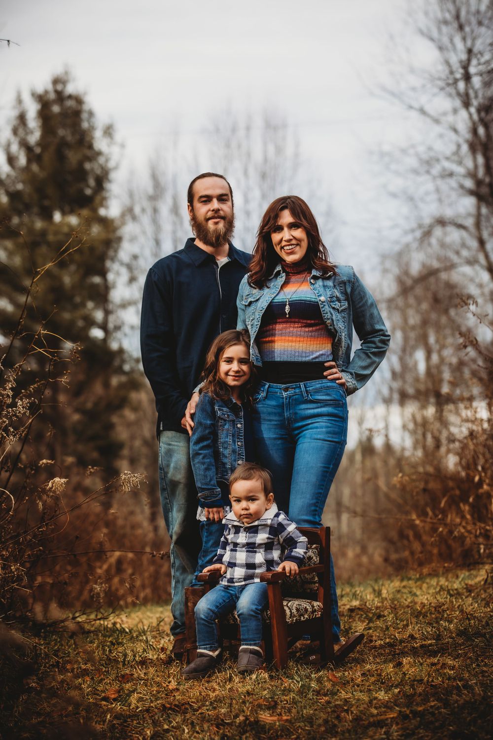 Family wearing denim and plaid stands together for autumn portrait in nature.