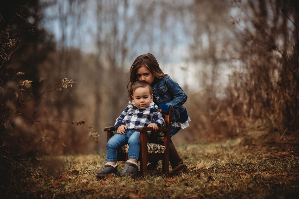 Playful outdoor portrait in autumn with child on rustic wooden chair.